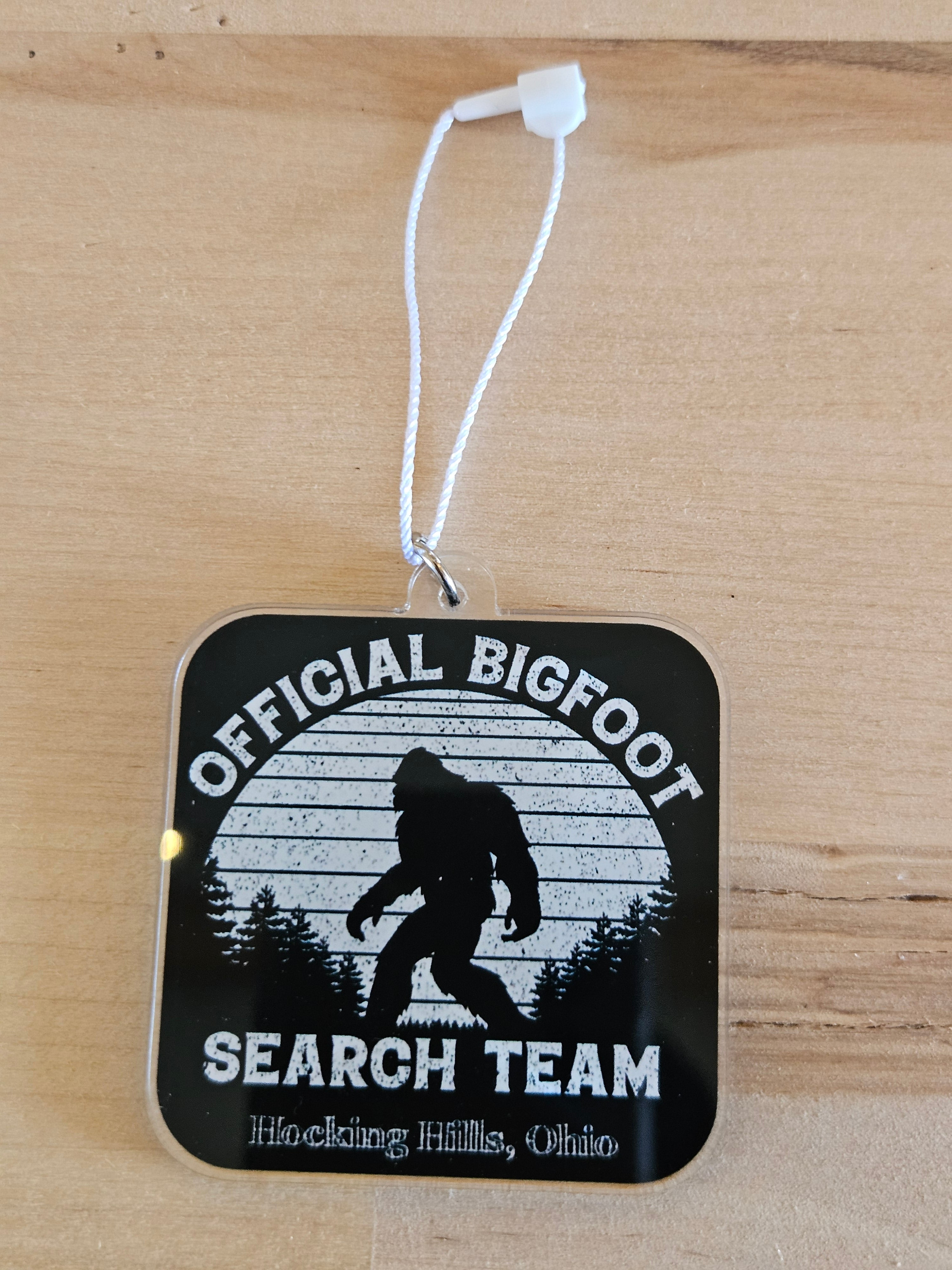 Black and white 'Official Bigfoot Search Team' tag on a wooden surface