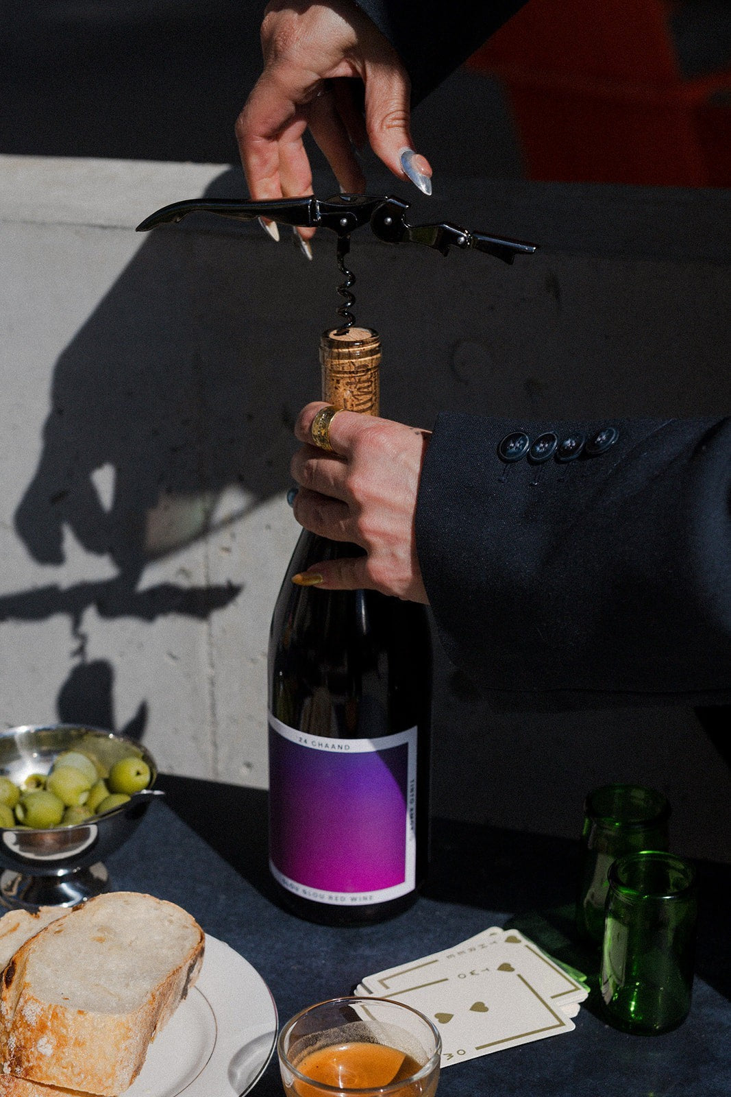 The Hocking Hills Store Chaand Glou Glou Red Wine bottle being opened with a corkscrew, served with bread and olives.