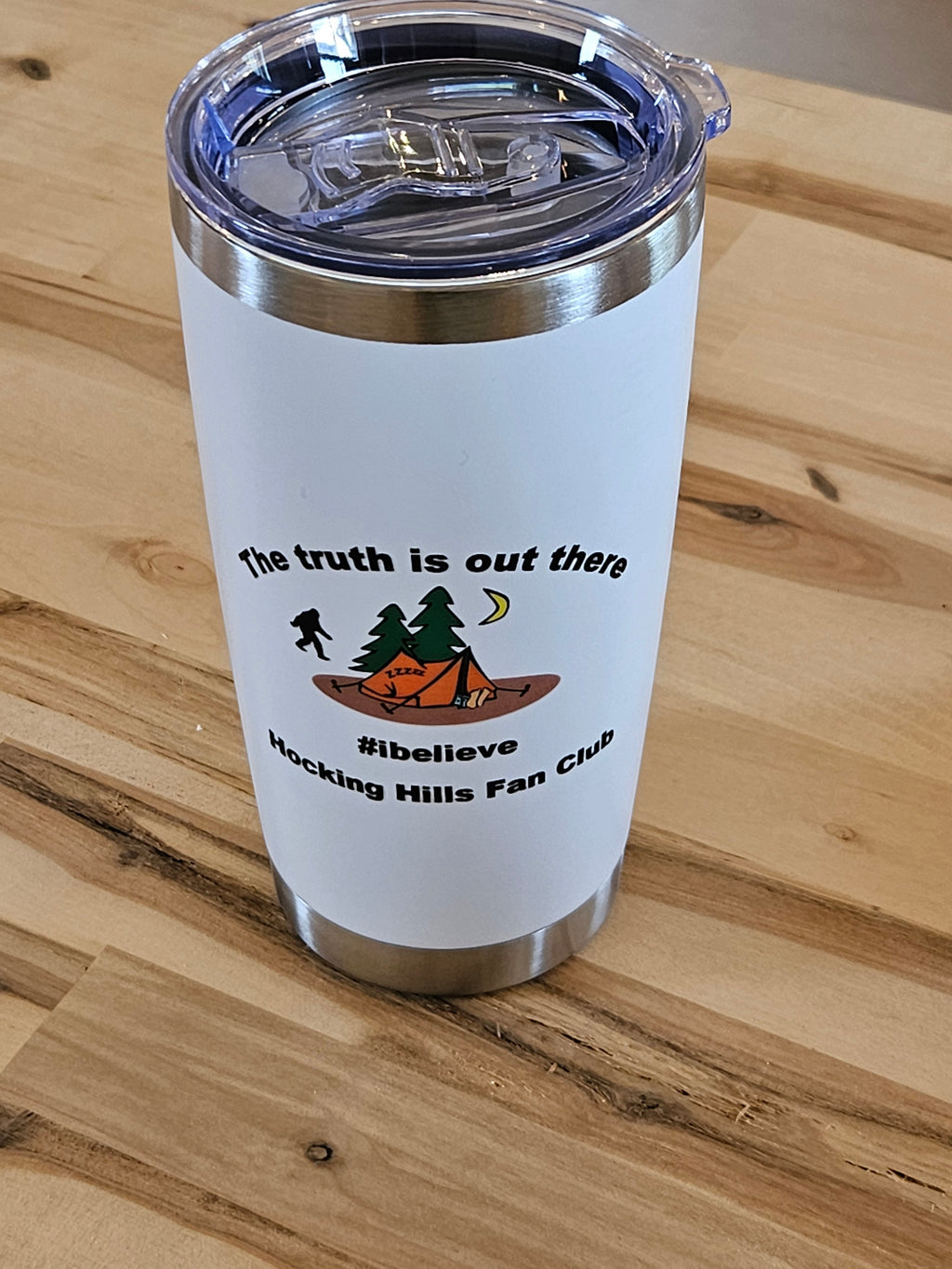 The Hocking Hills Store 20 oz white tumbler with Bigfoot, trees, tent, and moon graphic. "The truth is out there #ibelieve Hocking Hills Fan Club" text.