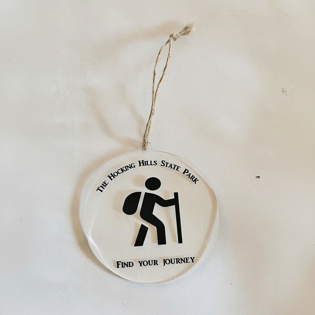 The Hocking Hills Store clear acrylic round ornament with a black hiker icon and text 'THE HOCKING HILLS STATE PARK FIND YOUR JOURNEY'.
