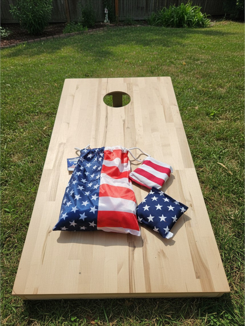 The Hocking Hills Store corn-hole bag set featuring American flag patterns on a wooden board in a grassy backyard.