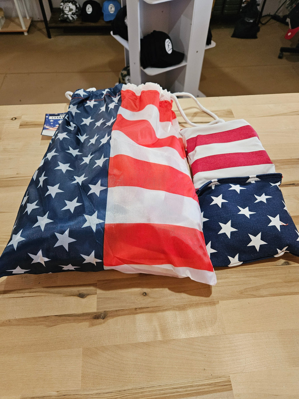 The Hocking Hills Store corn-hole bag set featuring red, white, and blue American flag patterns on a wooden table.