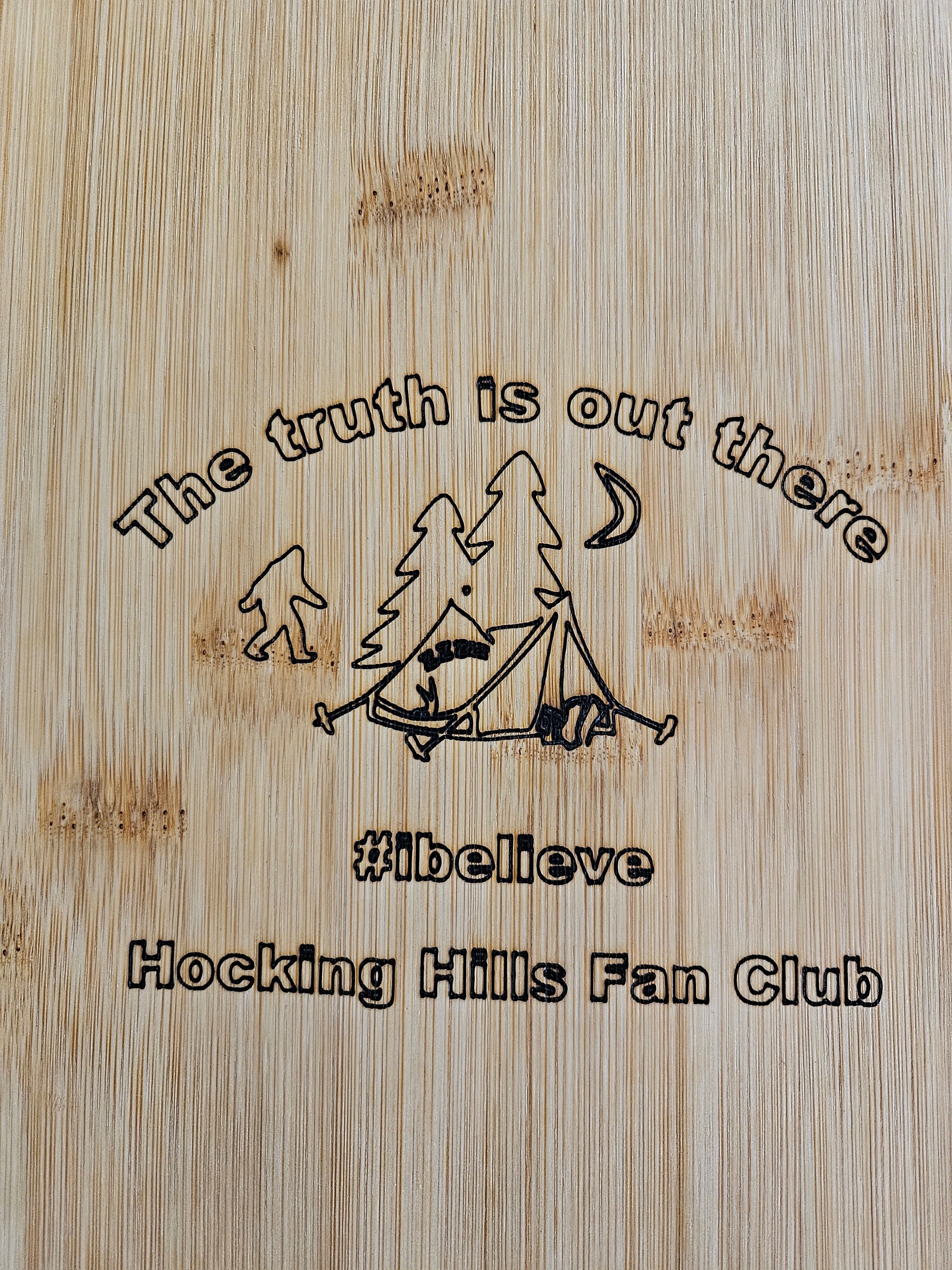 The Hocking Hills Store bamboo cutting board with Bigfoot, tent, trees, moon, and text "The truth is out there #ibelieve Hocking Hills Fan Club".