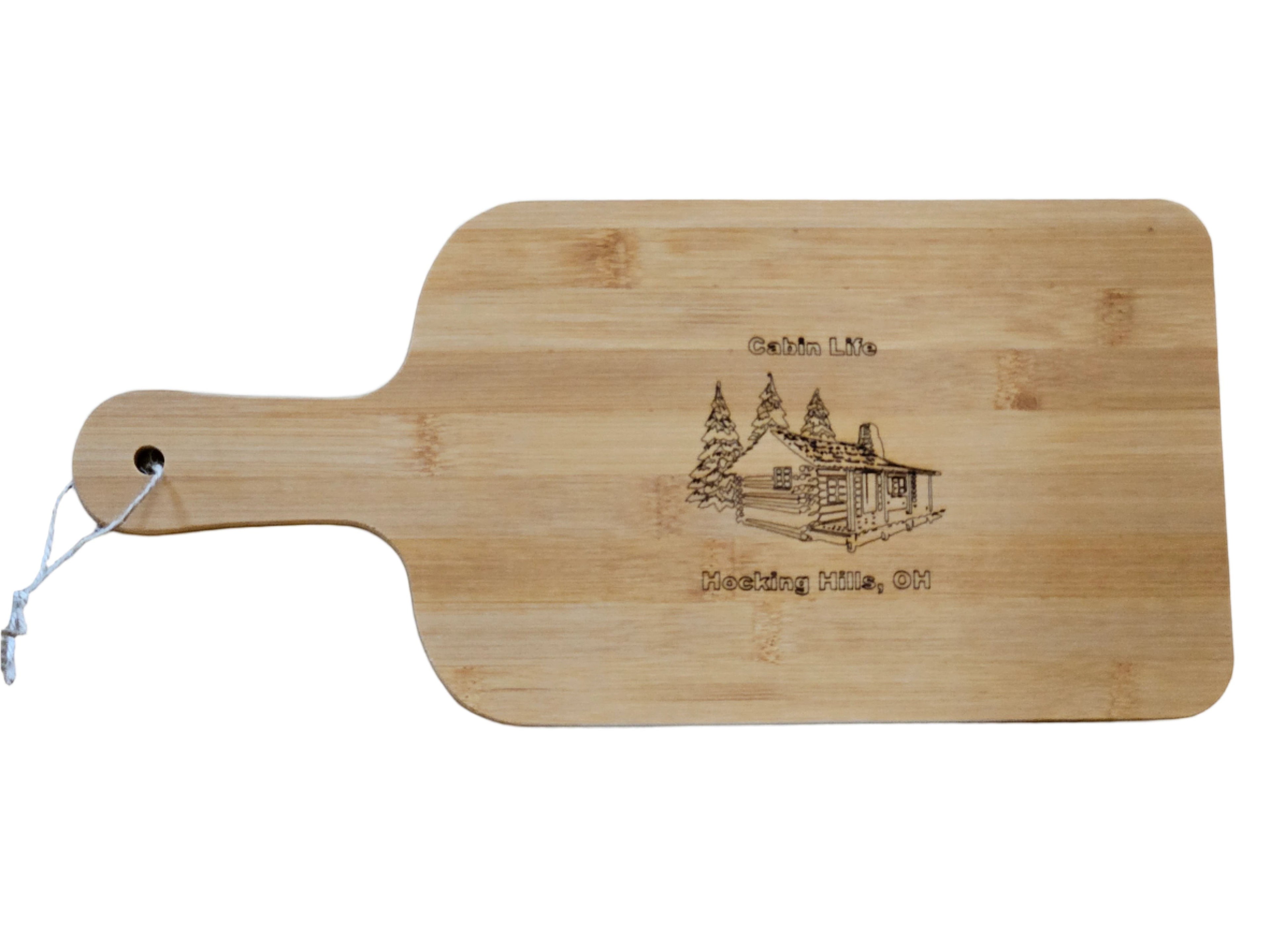 The Hocking Hills Store bamboo cutting board with laser engraved cabin and trees design. Features a handle with a hole for hanging.