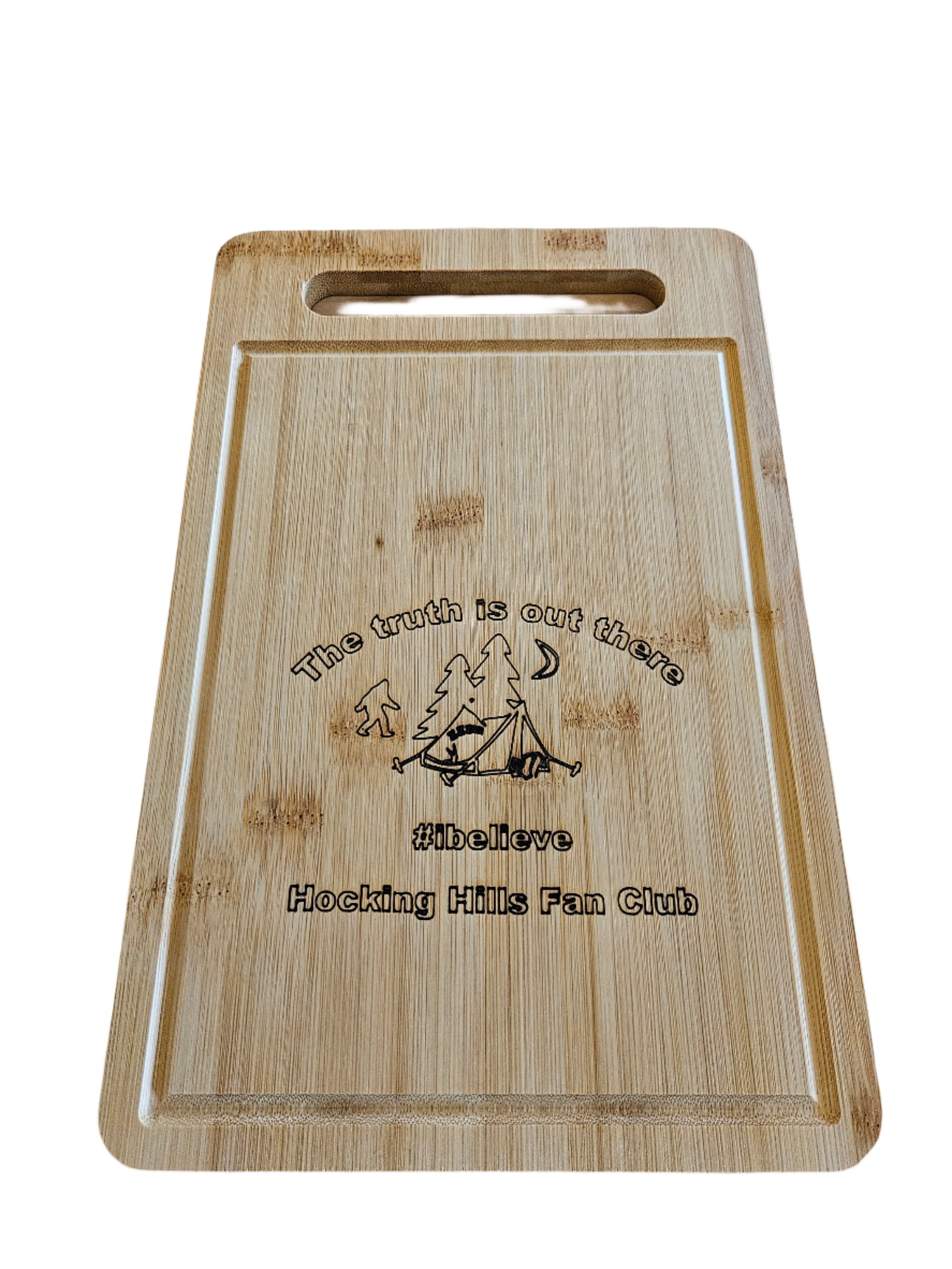 The Hocking Hills Store rectangle bamboo cutting board with Bigfoot, tent, and trees graphic. Features '#ibelieve Hocking Hills Fan Club' text.