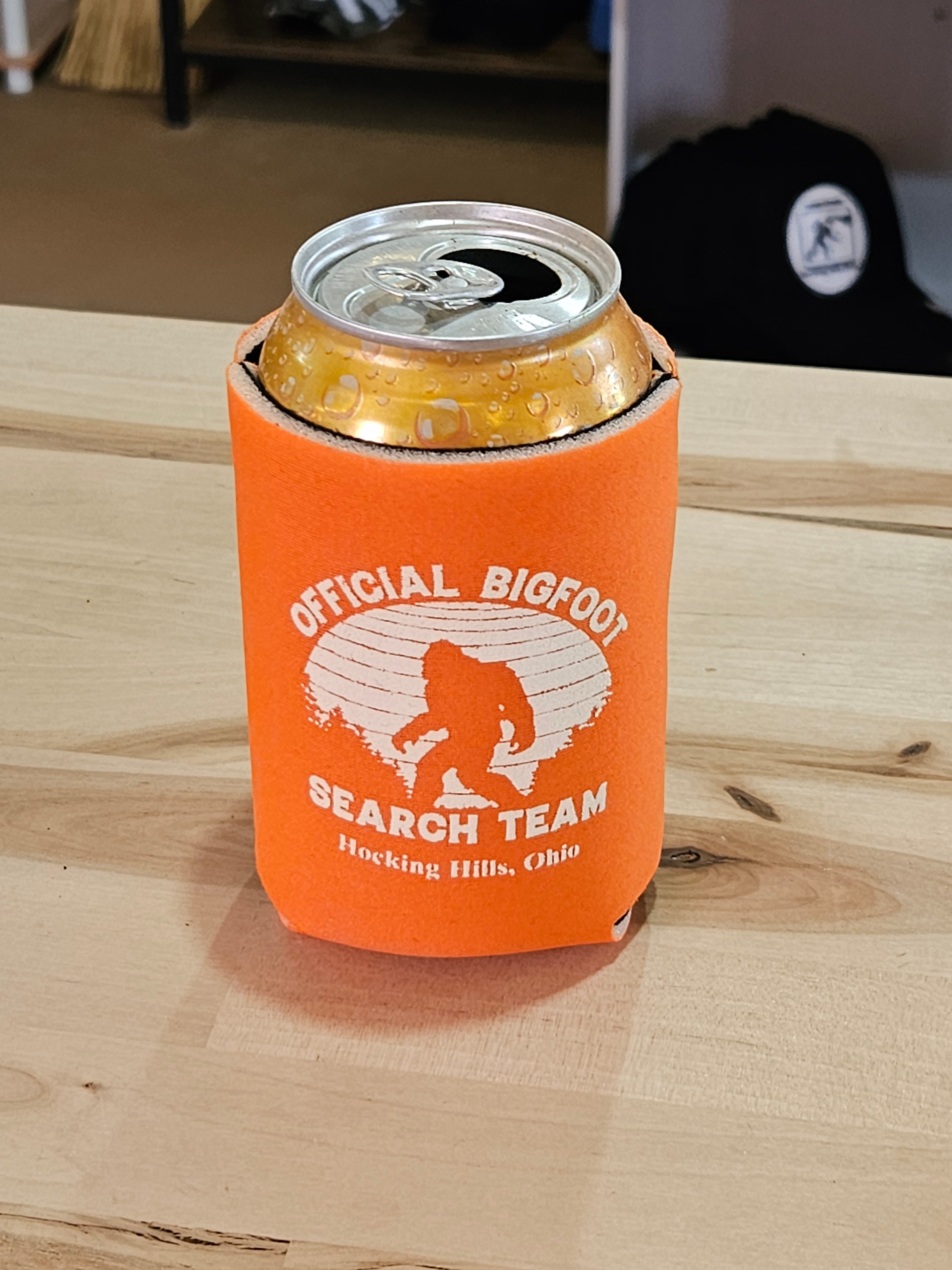 The Hocking Hills Store Official Bigfoot Search Team orange can cooler with a Bigfoot graphic and text.