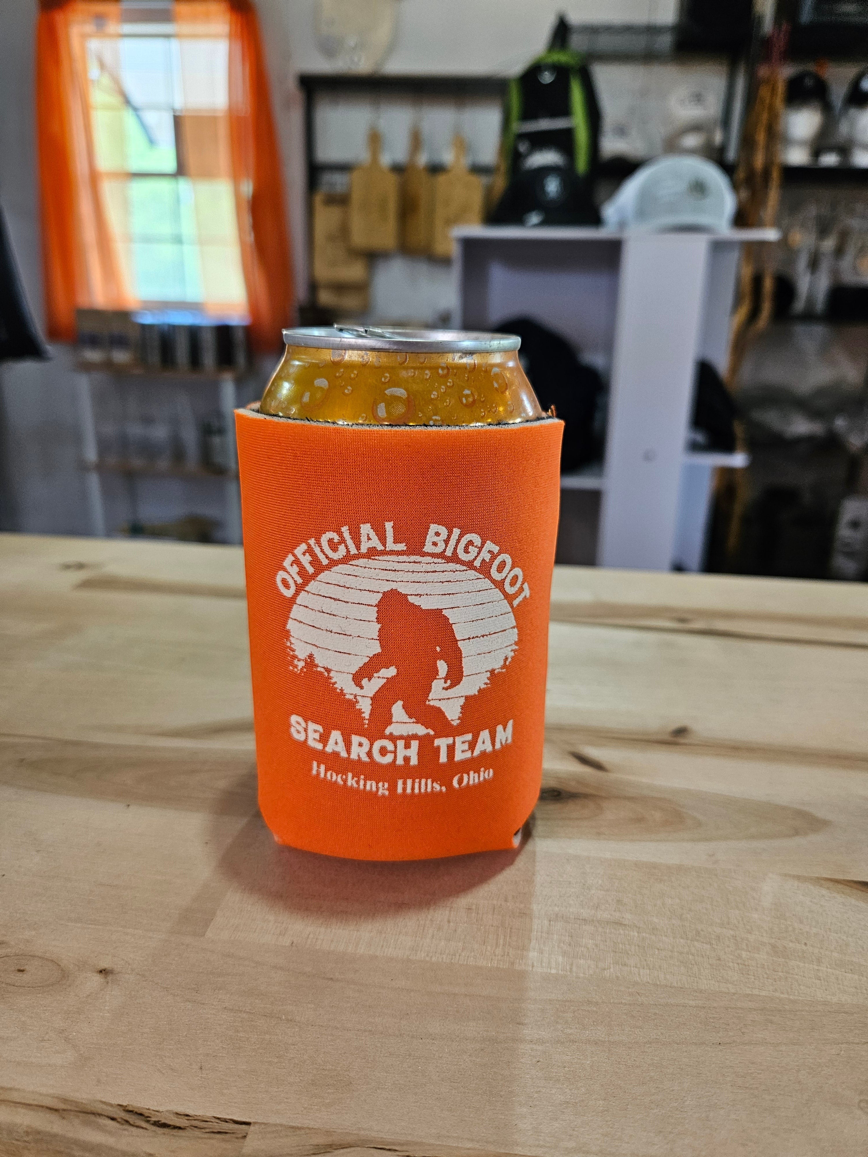 The Hocking Hills Store Official Bigfoot Search Team orange can cooler with Bigfoot graphic and text.