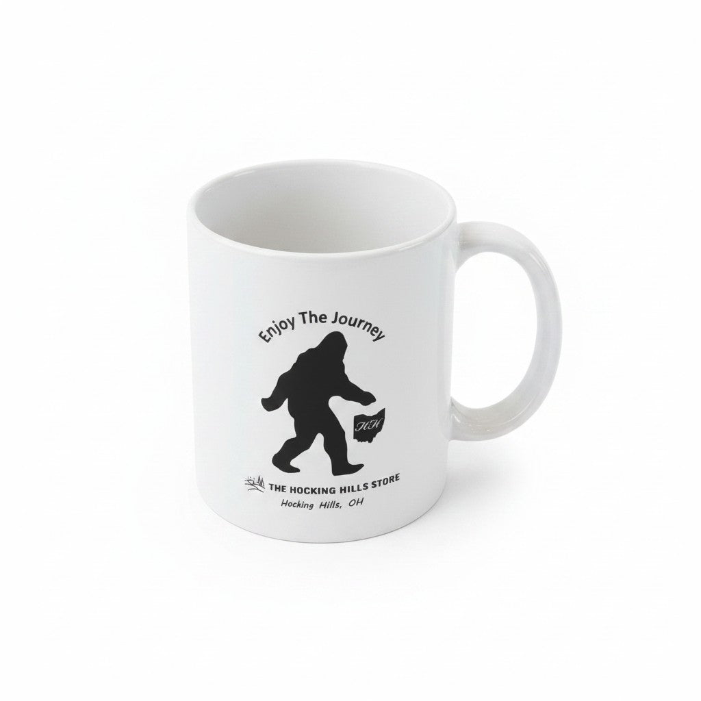 The Hocking Hills Store white ceramic coffee mug with a black Bigfoot silhouette and "Enjoy The Journey" text.