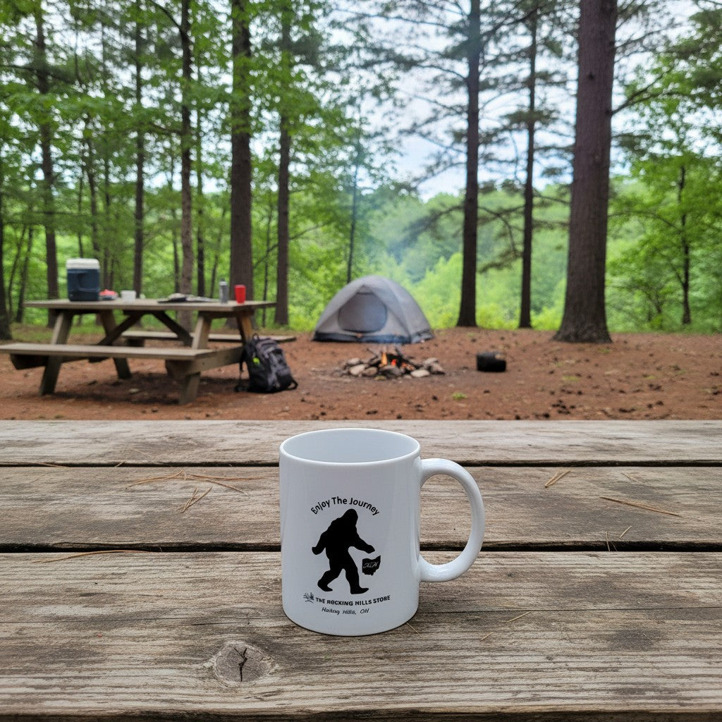 The Hocking Hills Store white ceramic coffee mug with a black Bigfoot silhouette and text "Enjoy The Journey".