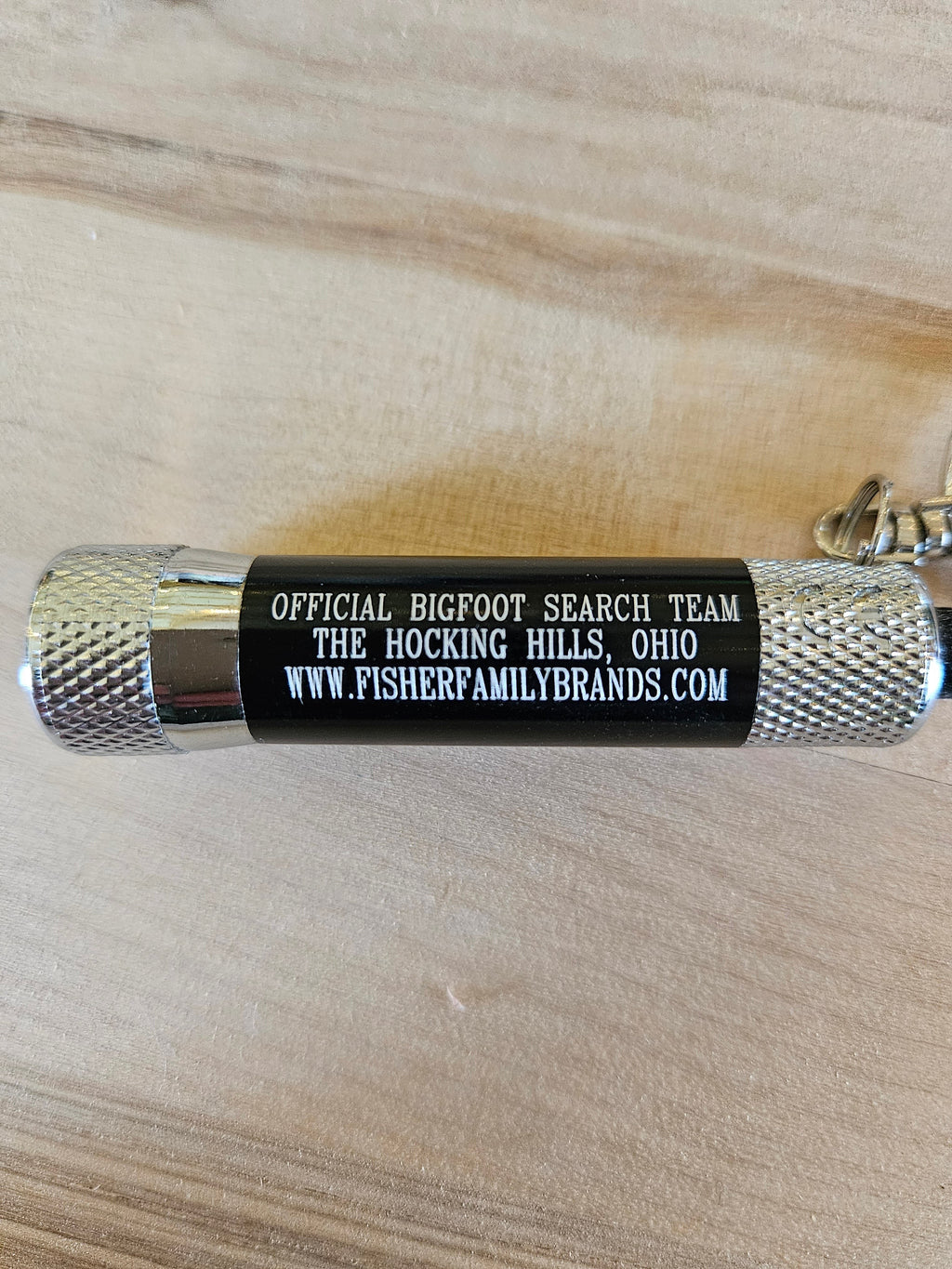 The Hocking Hills Store Bigfoot Search Team mini flashlight keychain with silver textured ends and black body.
