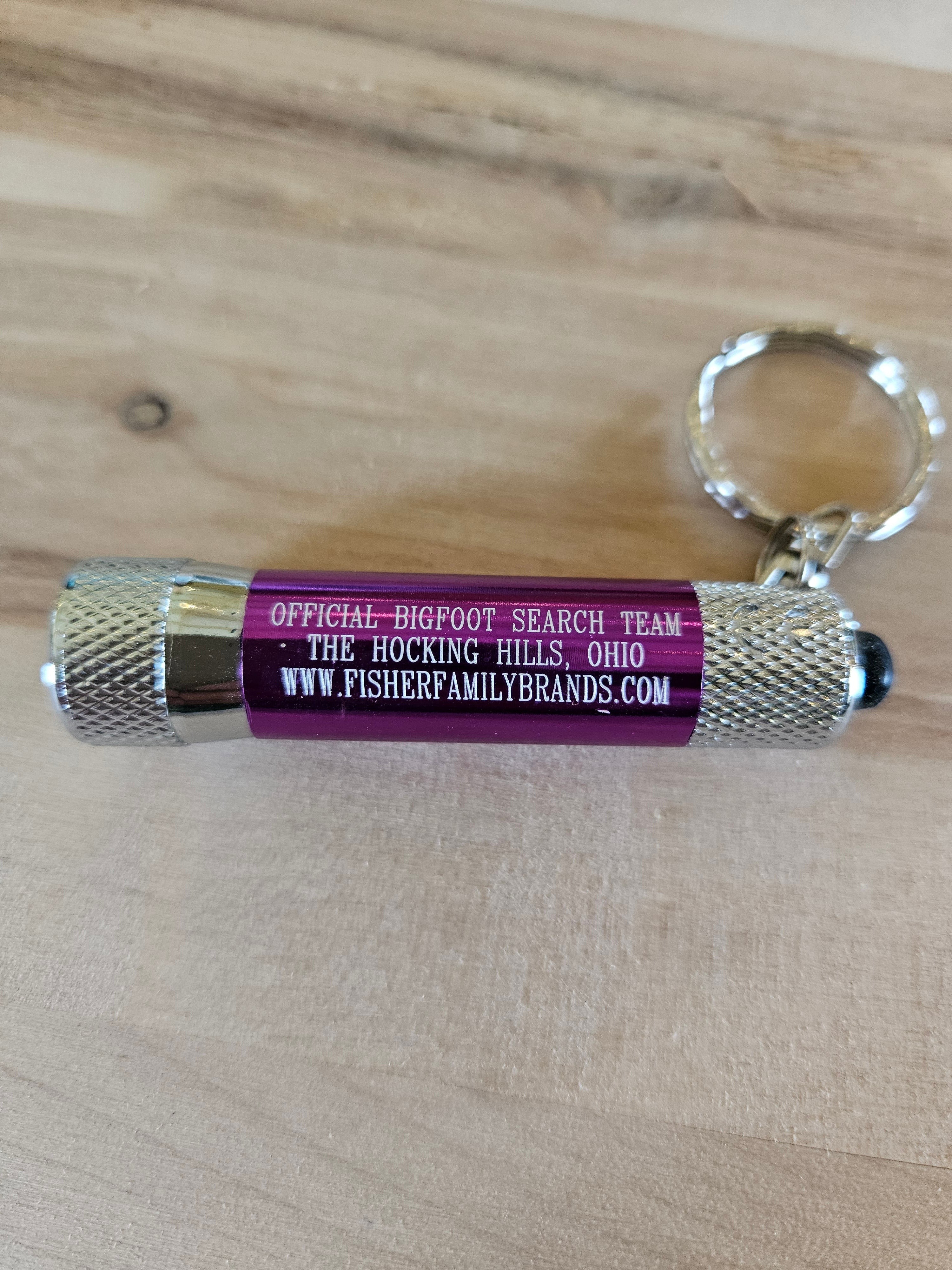 The Hocking Hills Store Bigfoot Search Team mini flashlight keychain with purple barrel and silver metal casing.