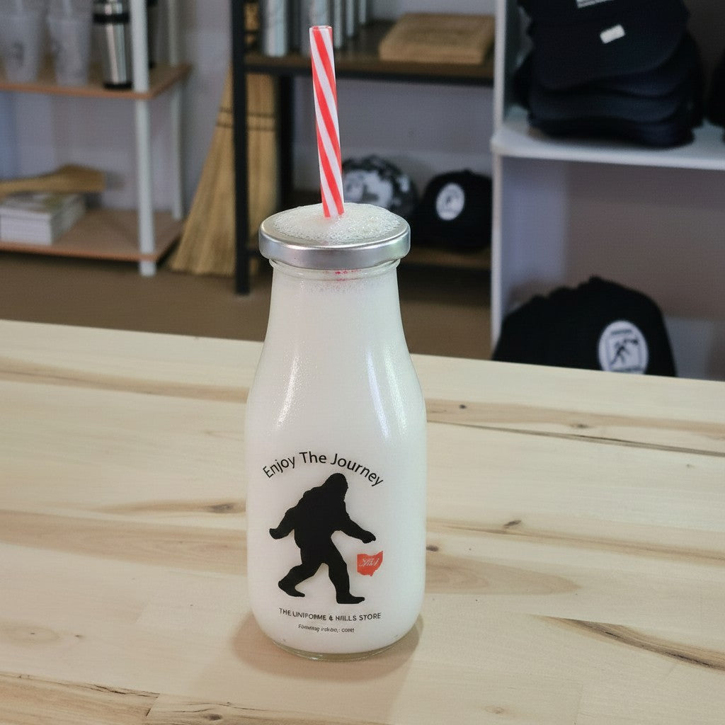 The Hocking Hills Store Bigfoot Enjoy The Journey glass milk bottle with red and white striped straw and metal lid, filled with iced tea.