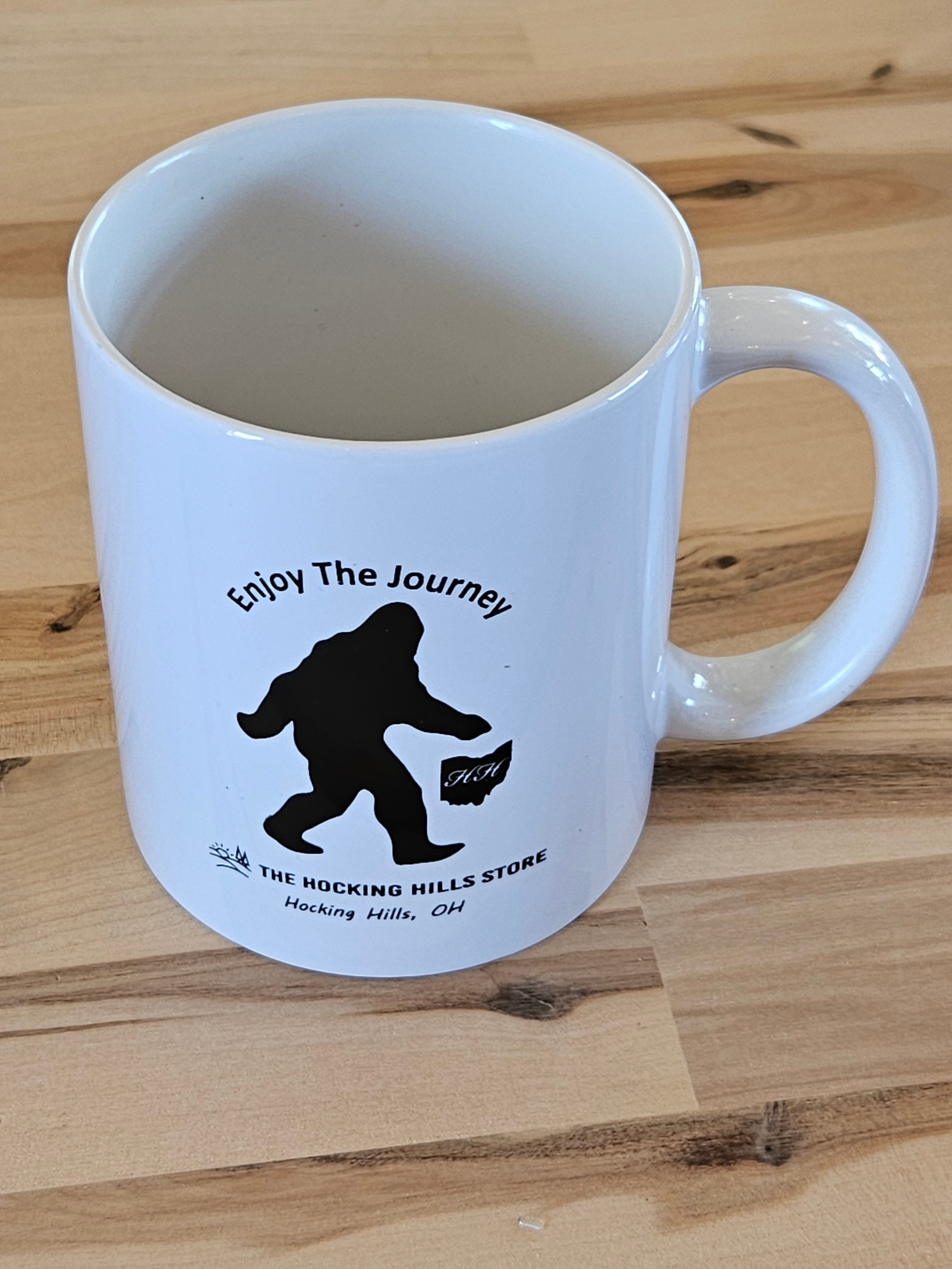 The Hocking Hills Store white ceramic mug with a black Bigfoot silhouette and "Enjoy The Journey" text.