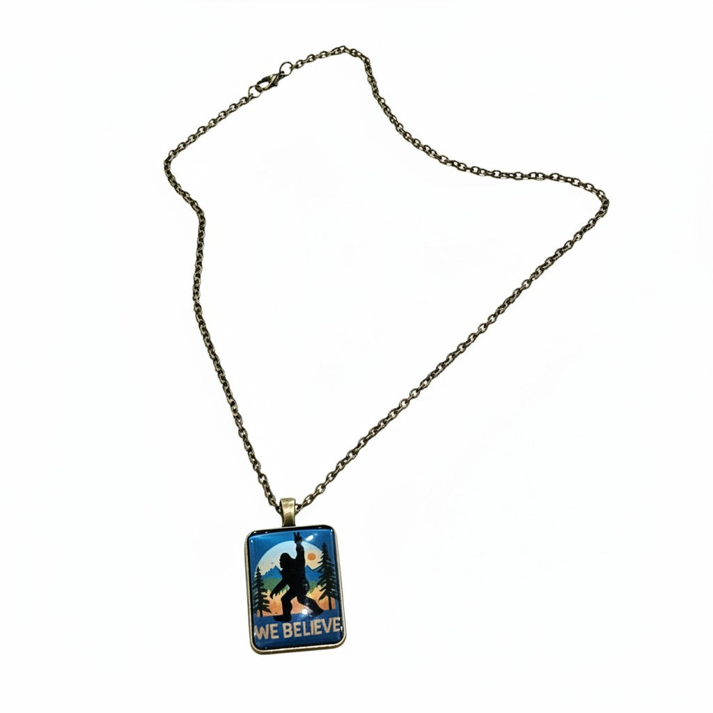The Hocking Hills Store Bigfoot We Believe pendant necklace with a silhouette of Bigfoot in a forest scene.