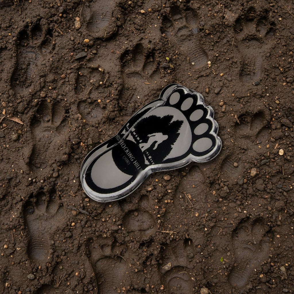 The Hocking Hills Store Bigfoot footprint pin, a silver-toned metal collectible with black Bigfoot silhouette and text.