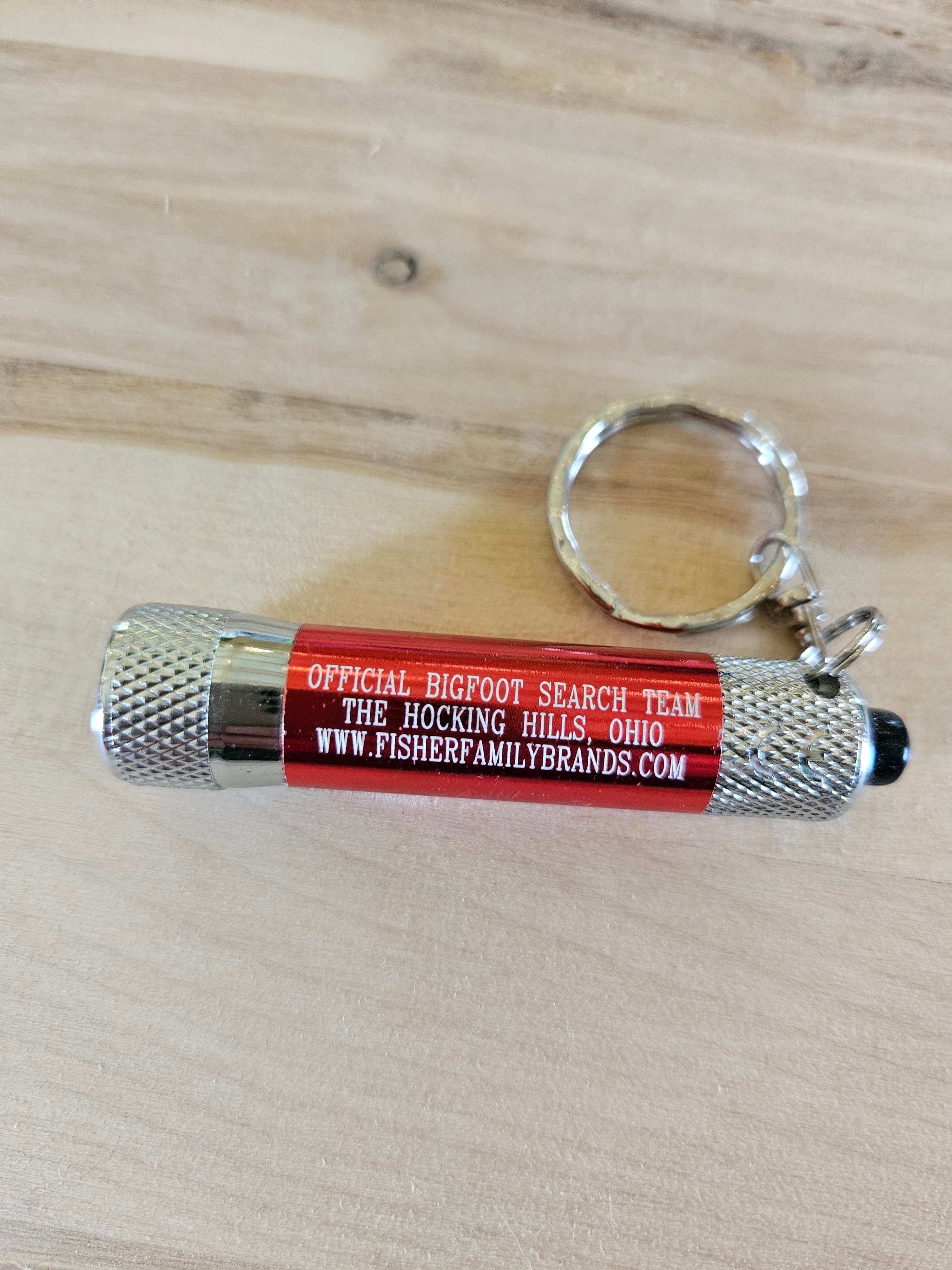 The Hocking Hills Store red metal Bigfoot Search Team keychain flashlight with silver accents and keyring.
