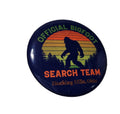 The Hocking Hills Store Official Bigfoot Search Team pin features a silhouette of Bigfoot against a sunset with trees and text.