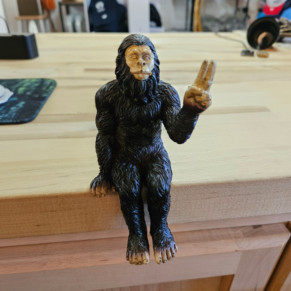 The Hocking Hills Store Bigfoot die-cast shelf sitting statue is dark brown with a tan face and hands, holding up two fingers.