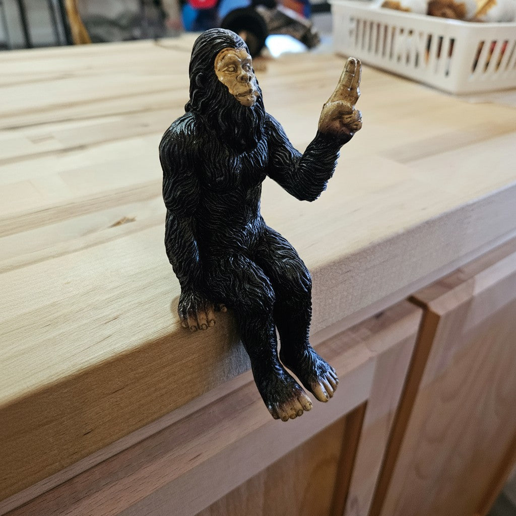 The Hocking Hills Store Bigfoot die-cast metal statue sits on a shelf, black fur, gold face, pointing finger.