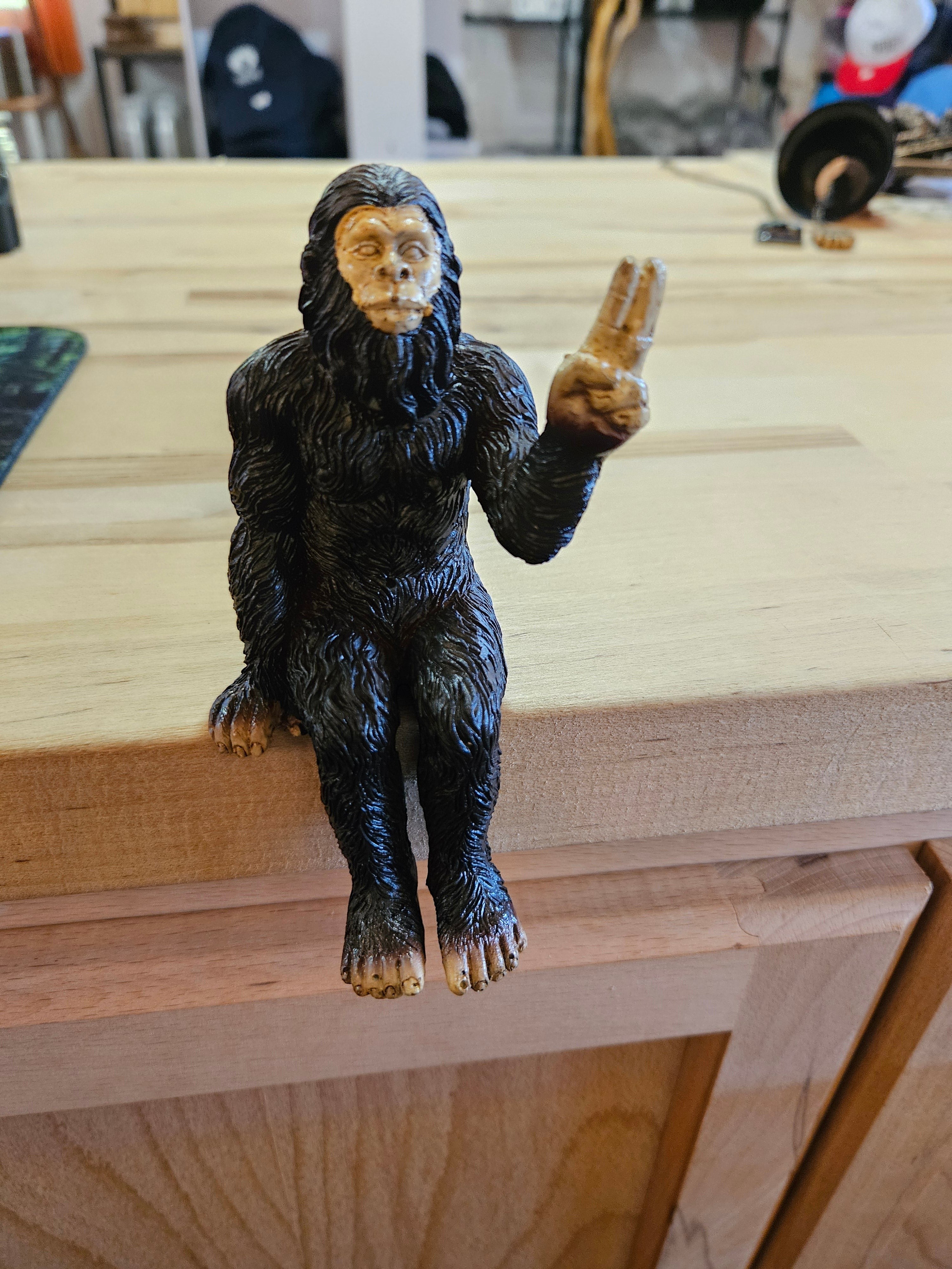 The Hocking Hills Store Bigfoot shelf sitting statue, dark brown, metal, with a peace sign gesture.