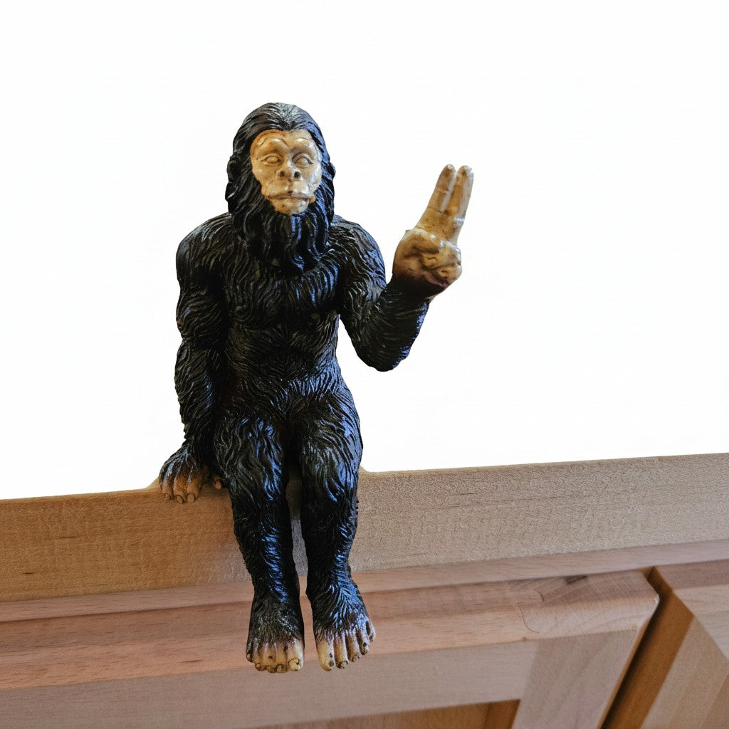 The Hocking Hills Store Bigfoot shelf sitting statue is a dark brown, furry figurine with a tan face and hands, giving a peace sign.