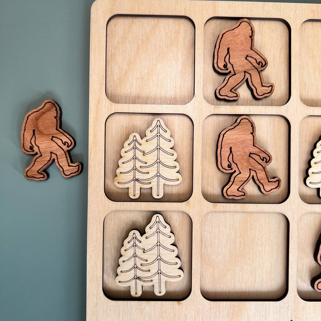 The Hocking Hills Store Bigfoot Tic-Tac-Toe game made of maple and cherry wood. Features Bigfoot and pine tree playing pieces.