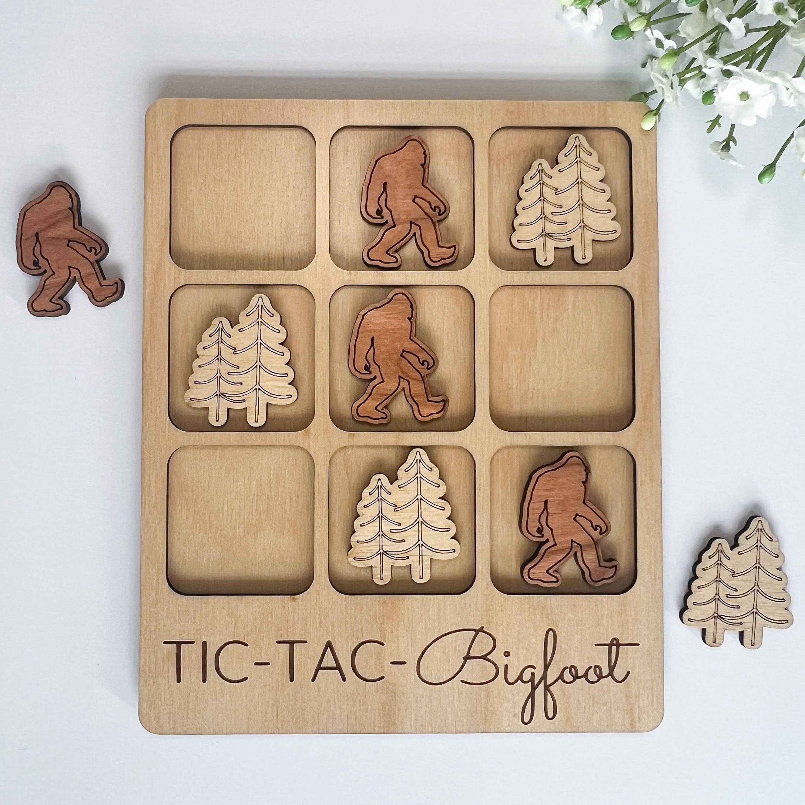 The Hocking Hills Store Bigfoot Tic-Tac-Toe game made of maple and cherry wood. Features Bigfoot and pine tree playing pieces.