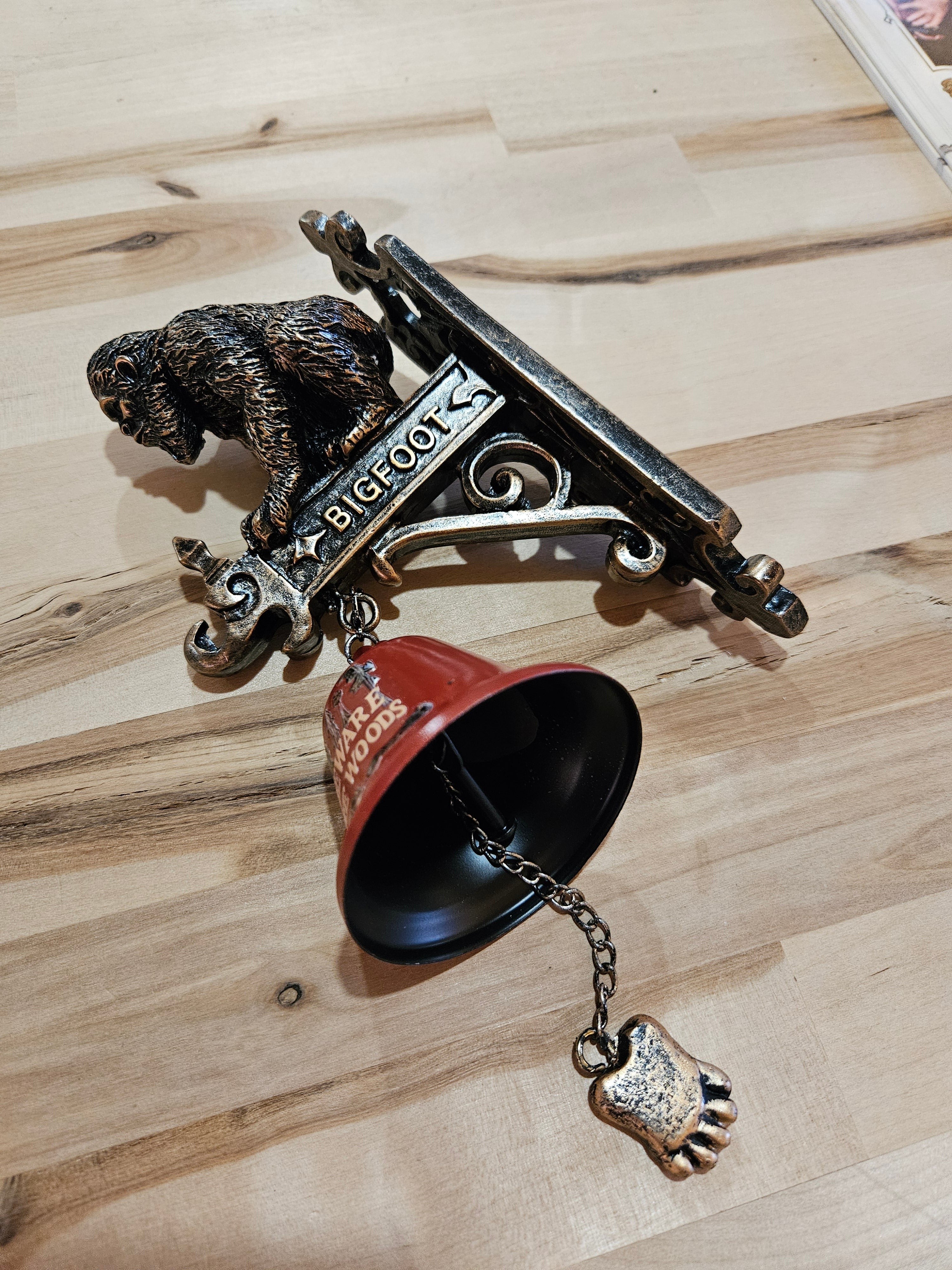 The Hocking Hills Store Bigfoot wall art and bell features a metal Bigfoot figure and a red bell with a Bigfoot foot charm.