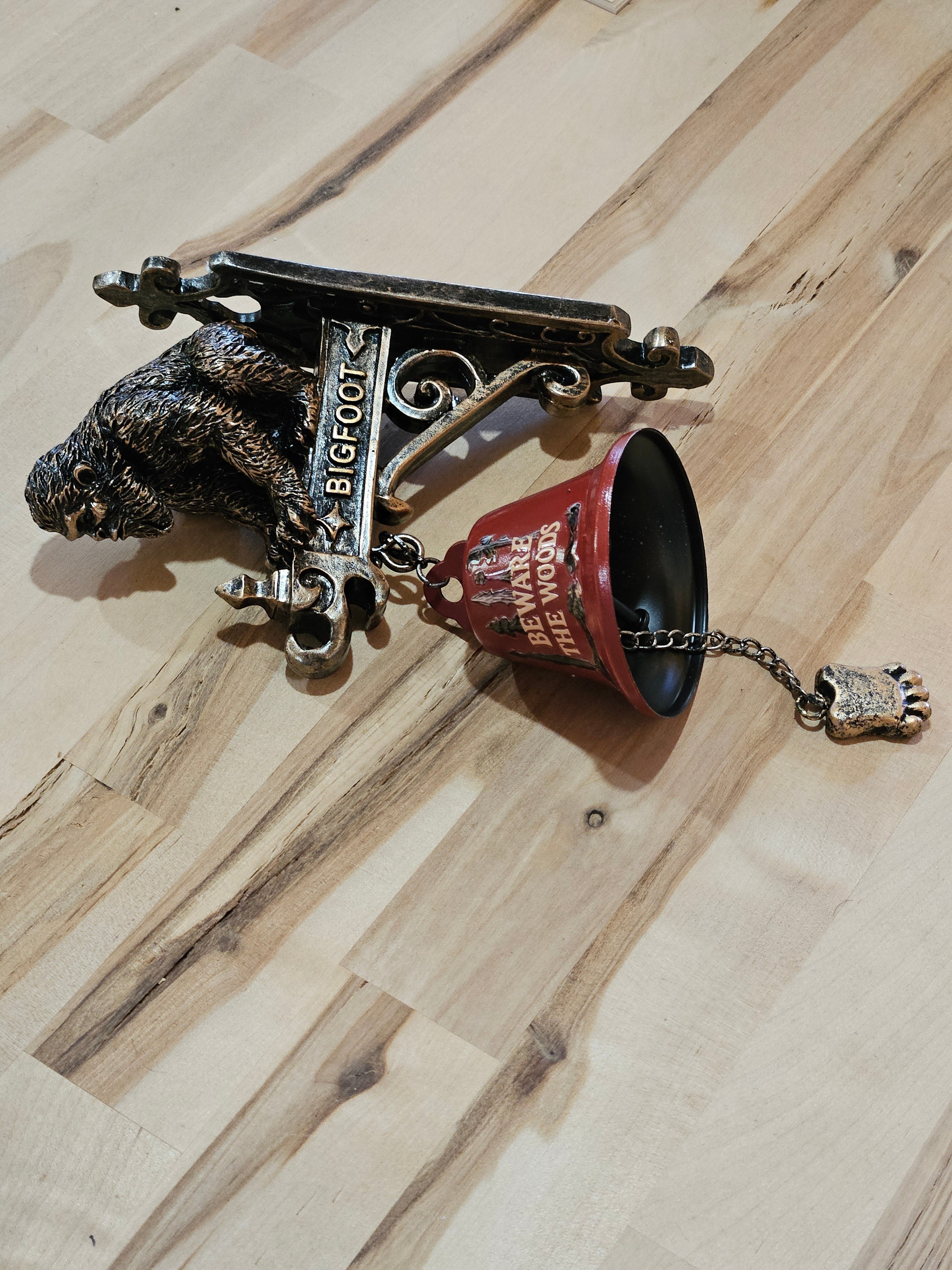 The Hocking Hills Store Bigfoot wall art and bell features a metal Bigfoot figure and a red bell with "Beware the Woods" text. Includes a Bigfoot foot pull chain.