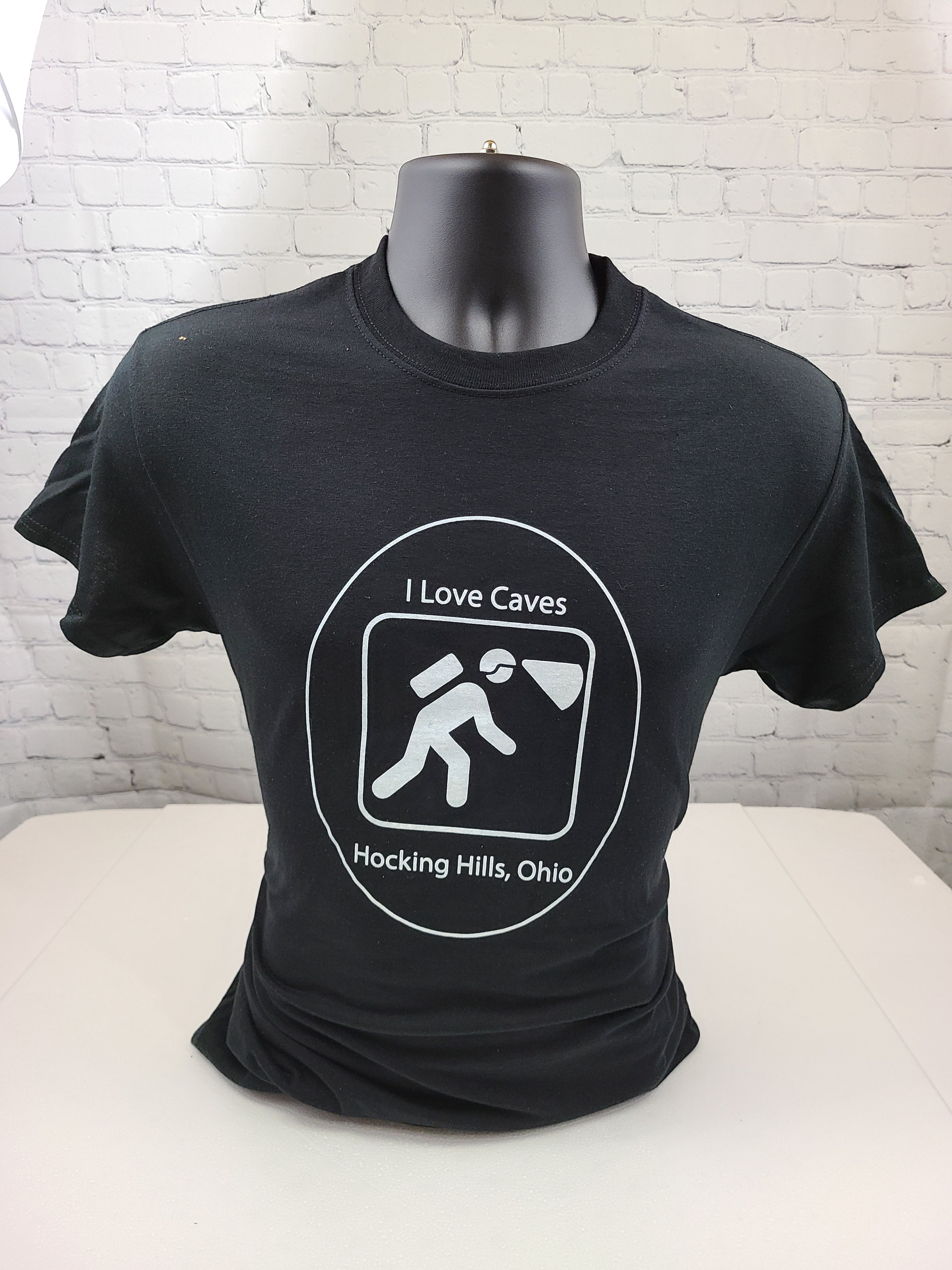 The Hocking Hills Store black cotton t-shirt with a white graphic that says "I Love Caves" and depicts a caver with a headlamp.