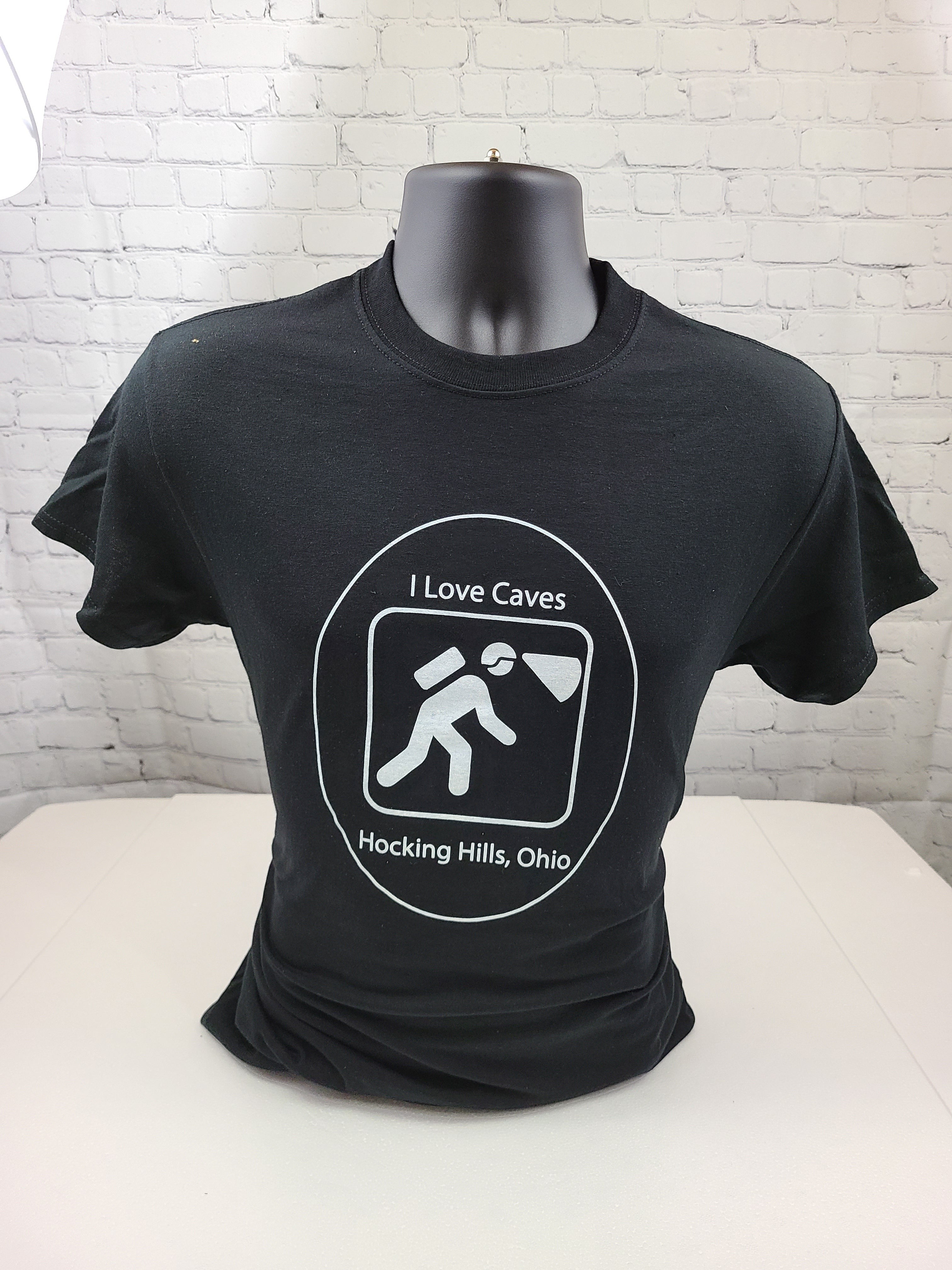 The Hocking Hills Store black cotton t-shirt with a white graphic of a caver exploring.