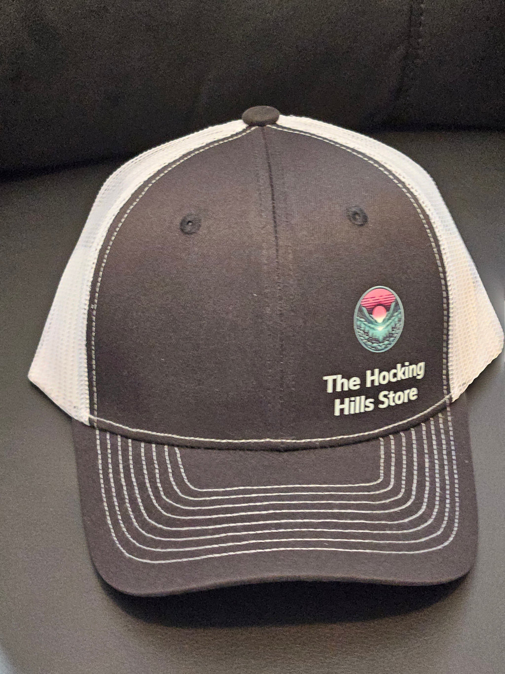 The Hocking Hills Store brown trucker hat with white mesh back and embroidered logo. Adjustable for a comfortable fit.