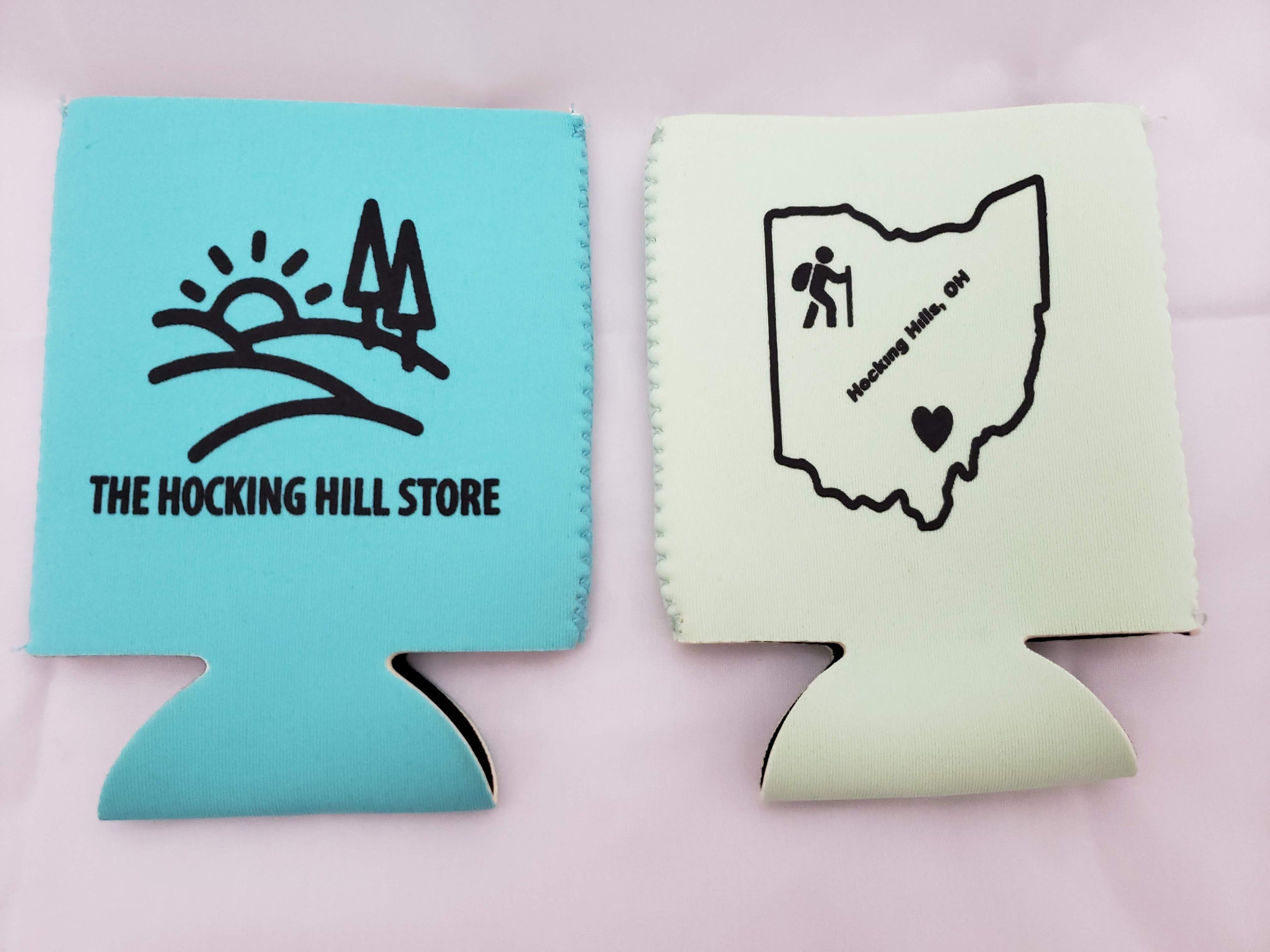 The Hocking Hills Store teal and light green can coolers. Teal cooler features a sunset and trees logo with store name. Light green cooler shows Ohio outline with hiker and Hocking Hills text.
