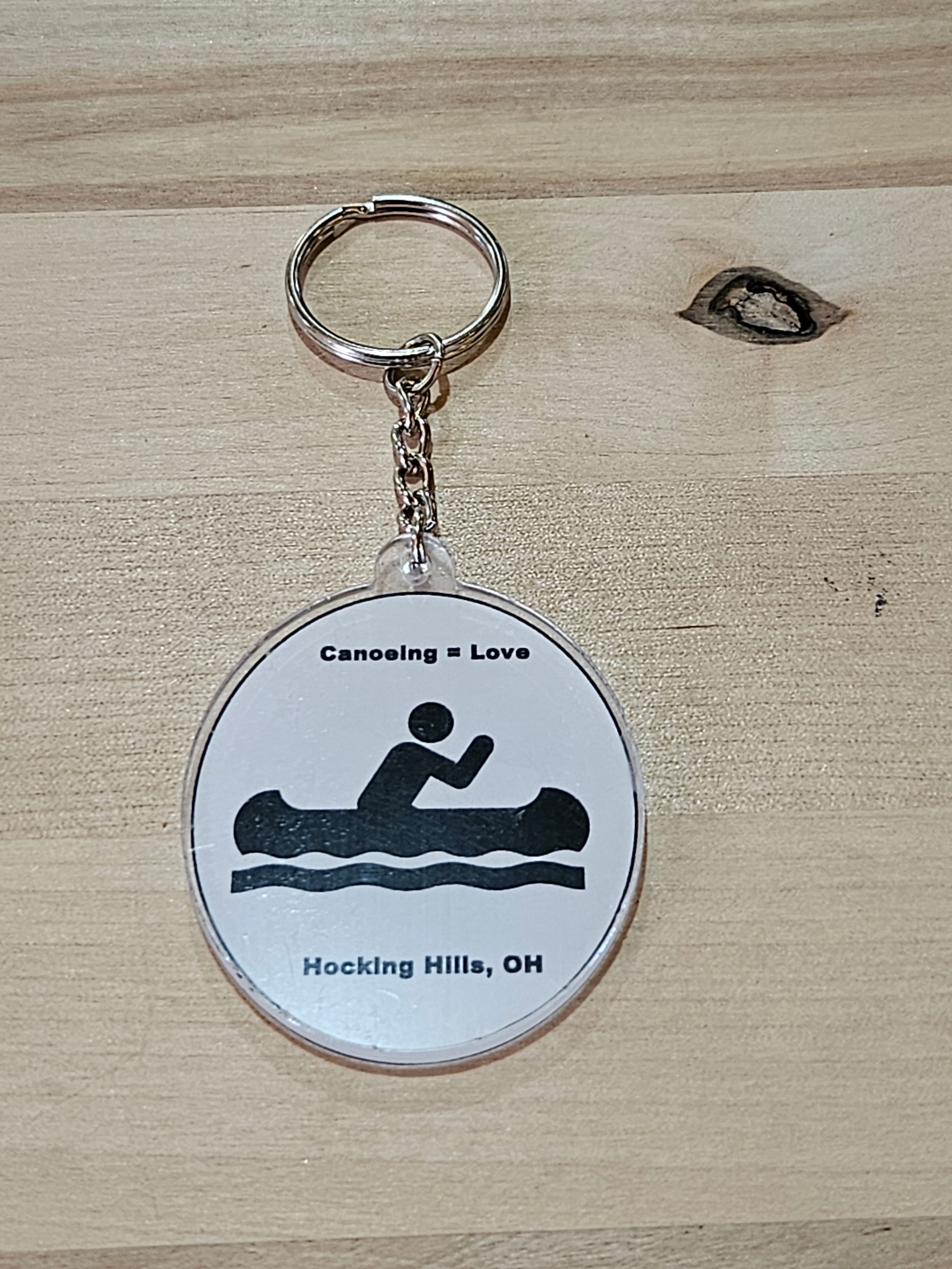 The Hocking Hills Store keychain with a circular design featuring a black silhouette of a person canoeing and the text "Canoeing = Love" and "Hocking Hills, OH".