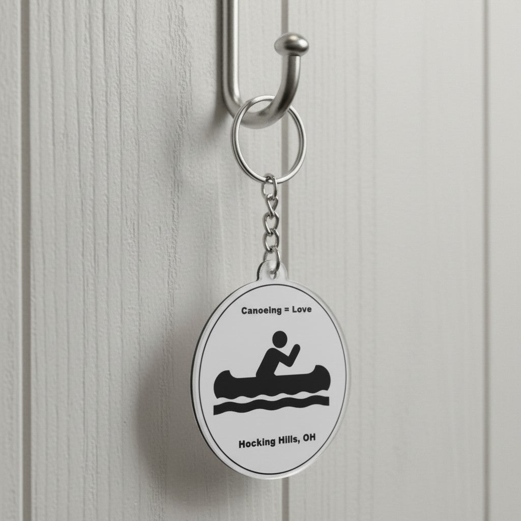 The Hocking Hills Store keychain with a circular design featuring a black silhouette of a person canoeing on waves, text reads 'Canoeing = Love' and 'Hocking Hills, OH'.