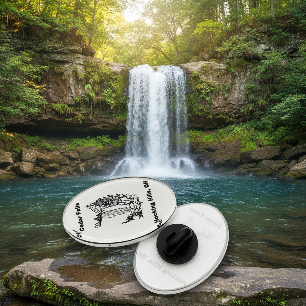 The Hocking Hills Store oval enamel pin featuring a black and white illustration of Cedar Falls waterfall and text.