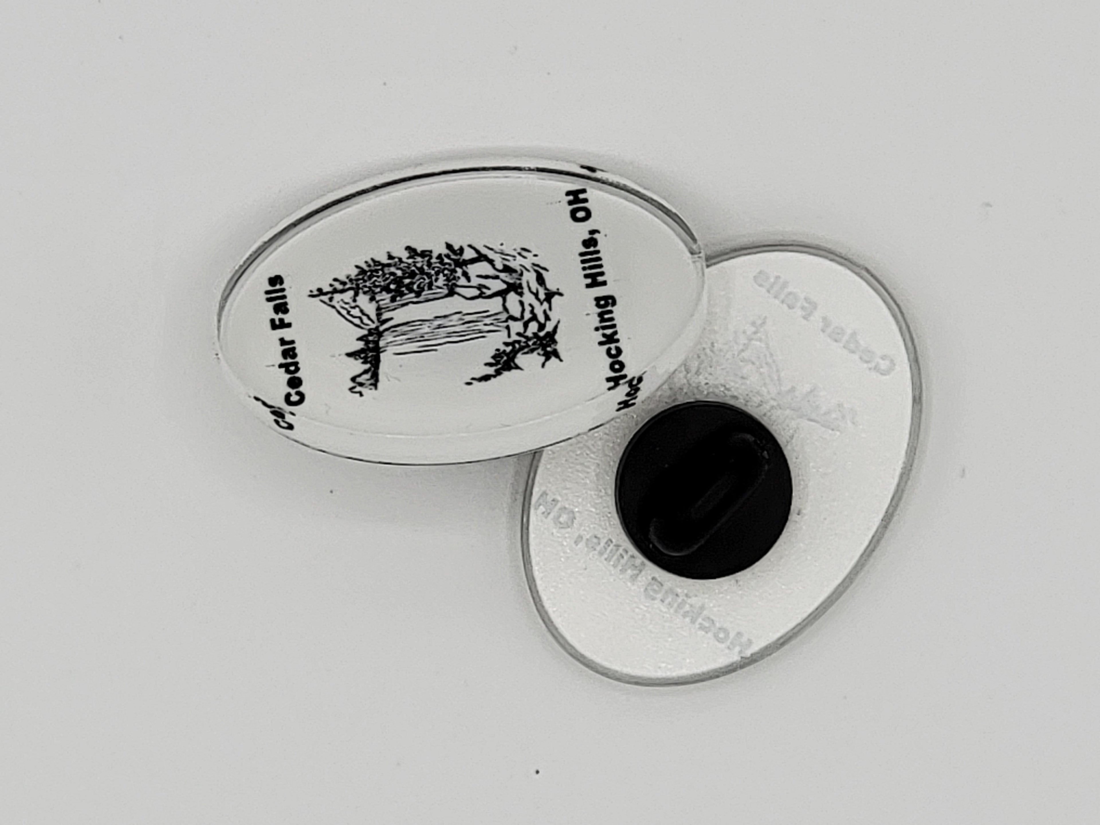 The Hocking Hills Store Cedar Falls oval pin featuring a black and white illustration of a waterfall and trees. Text reads "Cedar Falls Hocking Hills, OH".