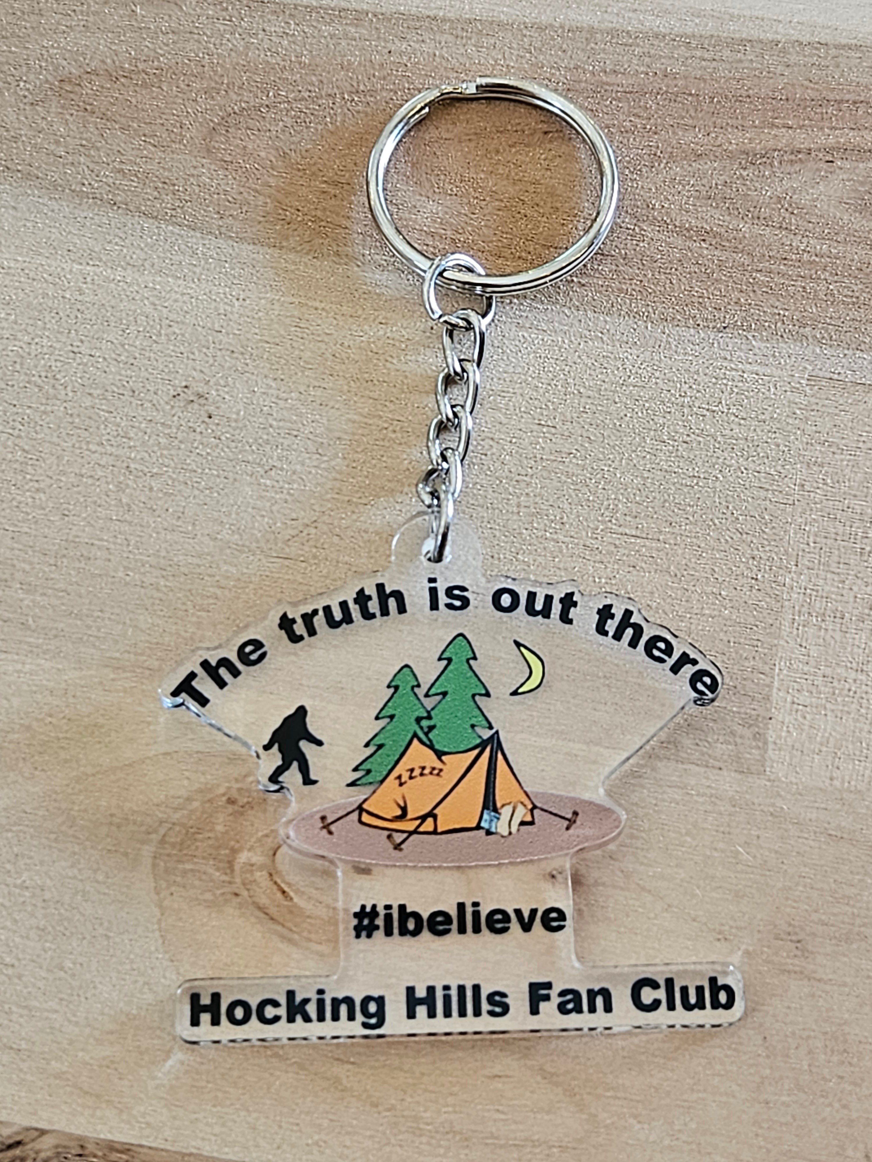 The Hocking Hills Store keychain with Bigfoot, tent, and trees. Features text 'The truth is out there', '#ibelieve', and 'Hocking Hills Fan Club'.