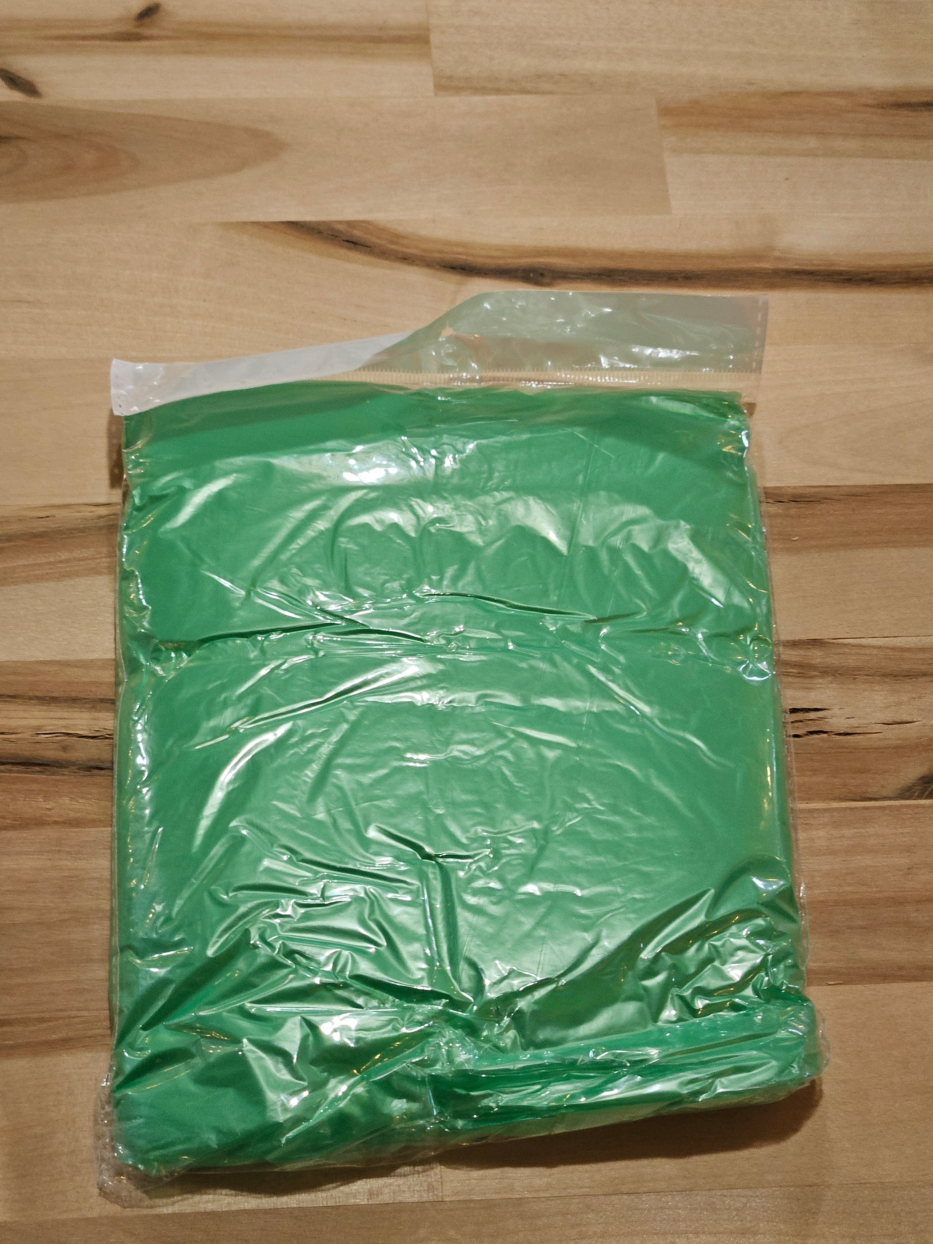 The Hocking Hills Store green disposable emergency rain poncho in clear plastic packaging on a wooden surface.