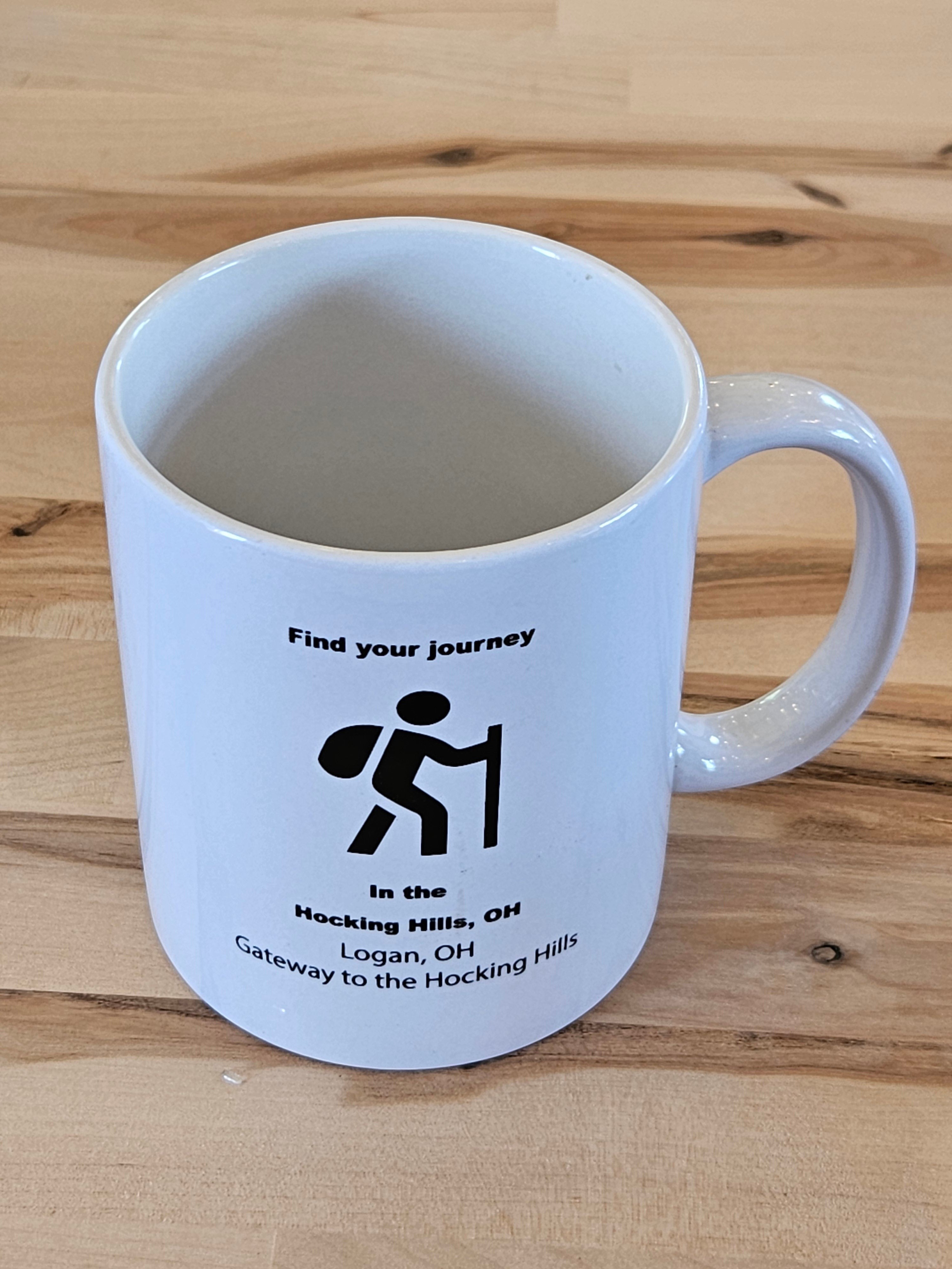The Hocking Hills Store white ceramic mug with black text and hiker graphic. Features "Find your journey" and location details.