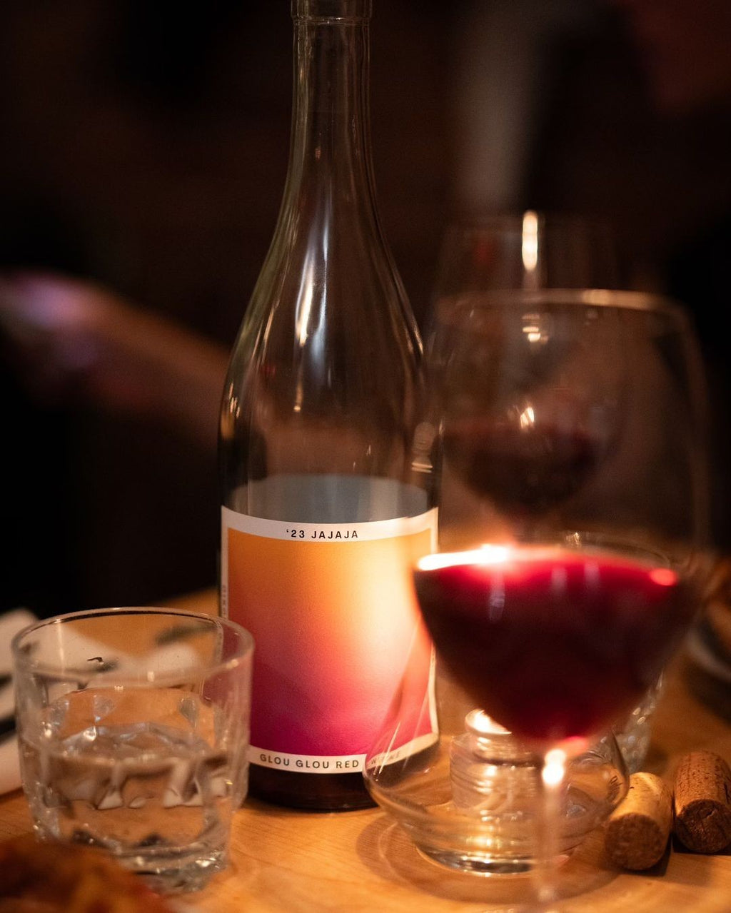 The Hocking Hills Store Jajaja Glou Glou Red wine bottle with a gradient label, next to a glass of red wine and a glass of water.