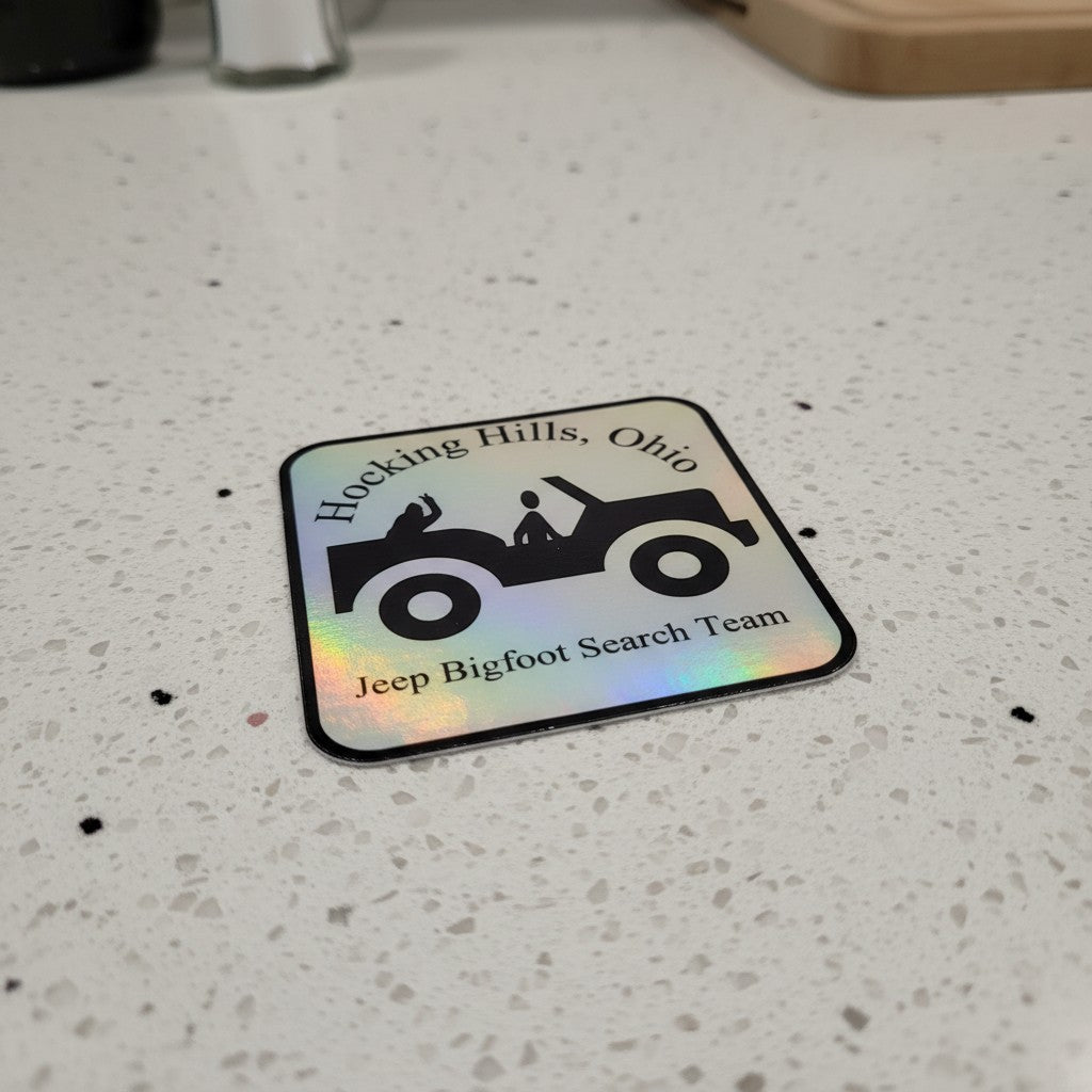 The Hocking Hills Store holographic bumper sticker featuring a black silhouette of a Jeep with two figures and text "Hocking Hills, Ohio Jeep Bigfoot Search Team."