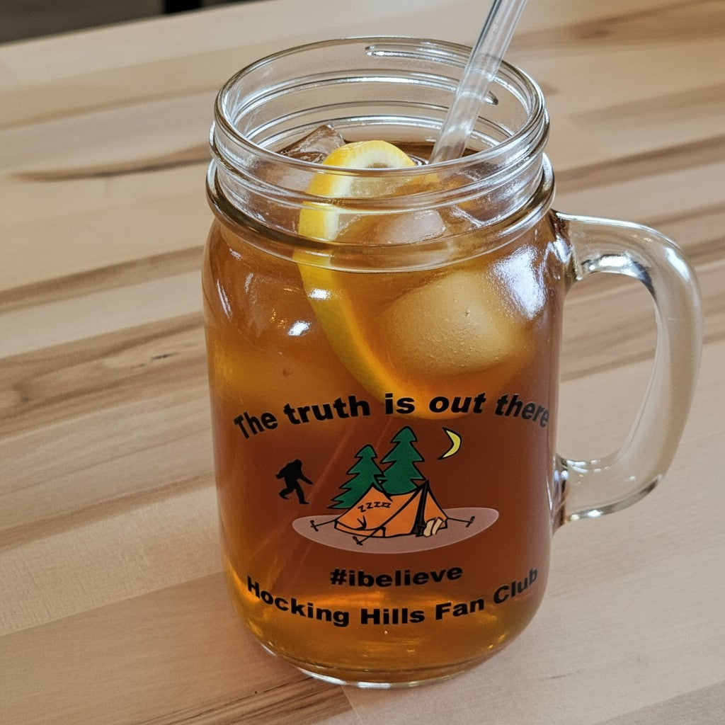 The Hocking Hills Store clear glass mason jar with handle, featuring a camping scene graphic and "The truth is out there #ibelieve Hocking Hills Fan Club" text.