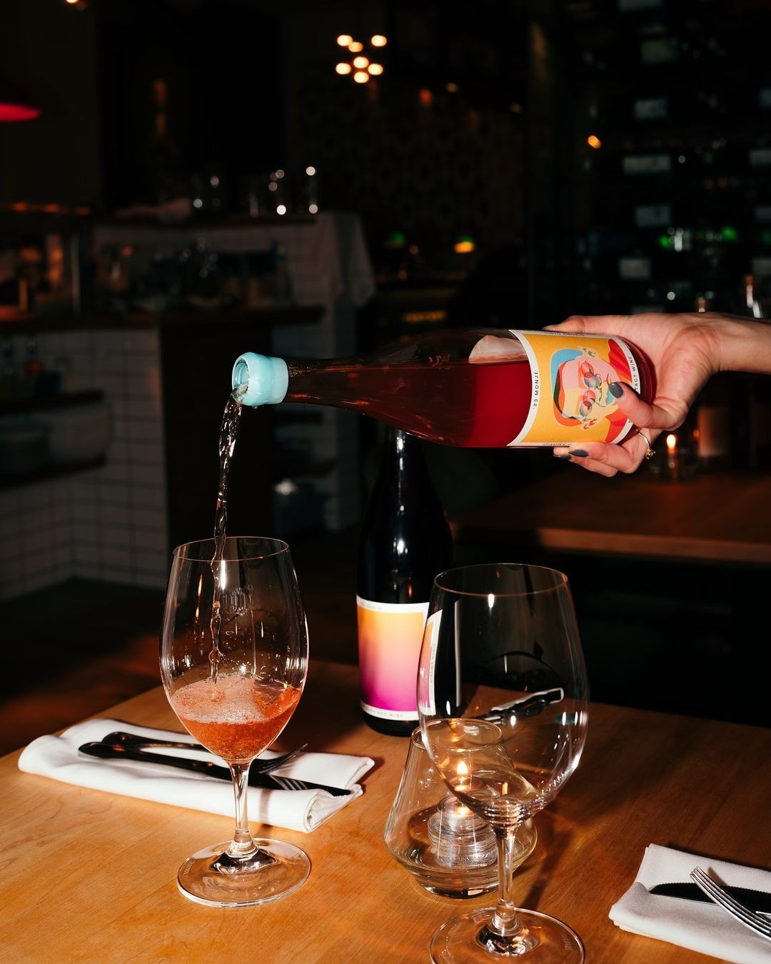 The Hocking Hills Store Natural Wine Sampler: A hand pours rosé wine into a glass at a table setting with two wine glasses and a candle.