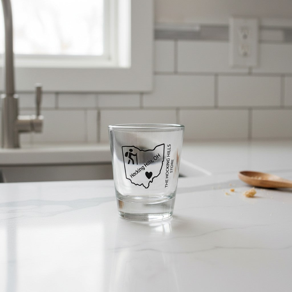 The Hocking Hills Store clear glass shot glass featuring an outline of Ohio with "Hocking Hills, OH" text and a hiker icon.