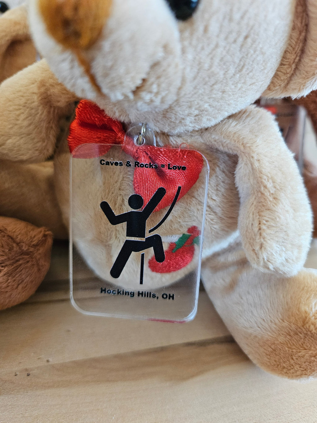 The Hocking Hills Store light brown plush bear with a red bow tie and a clear tag featuring a rock climber graphic.