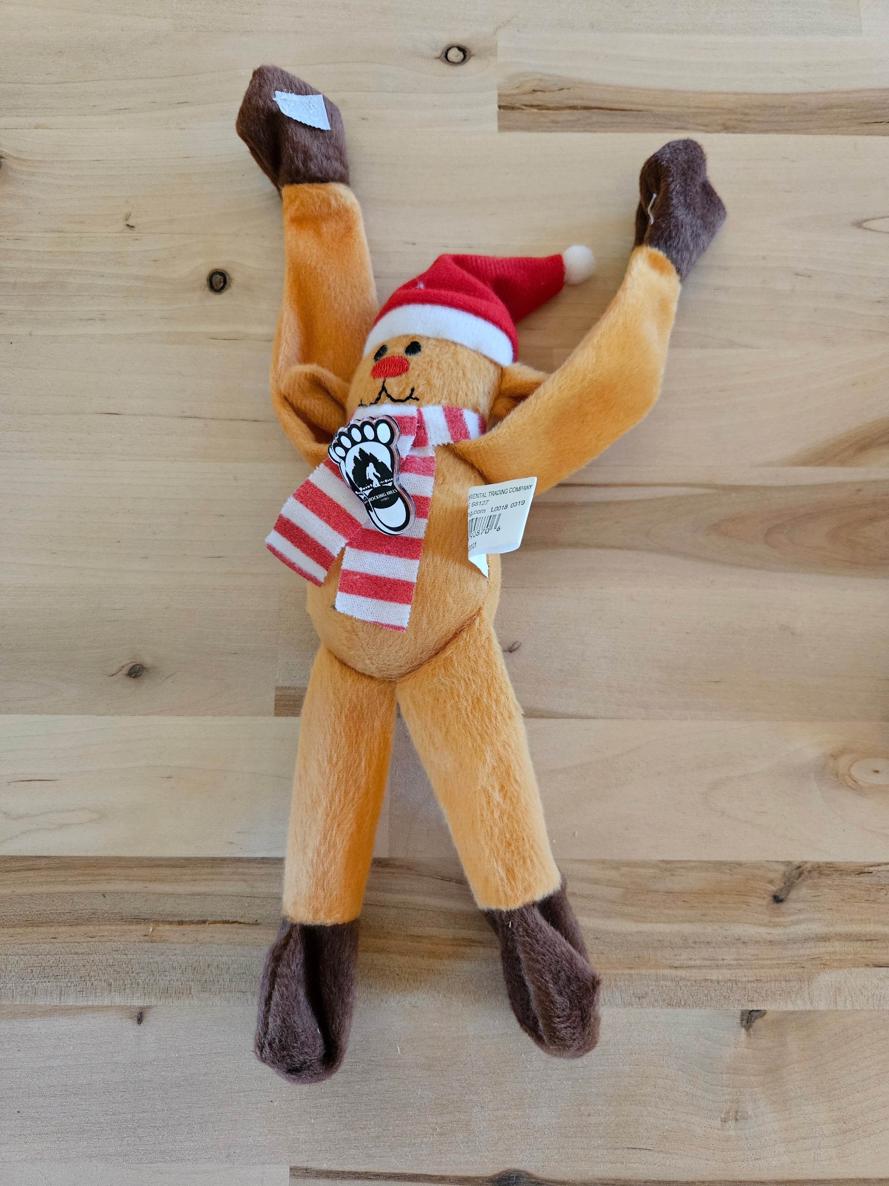 The Hocking Hills Store plush reindeer with red Santa hat and striped scarf, arms raised.