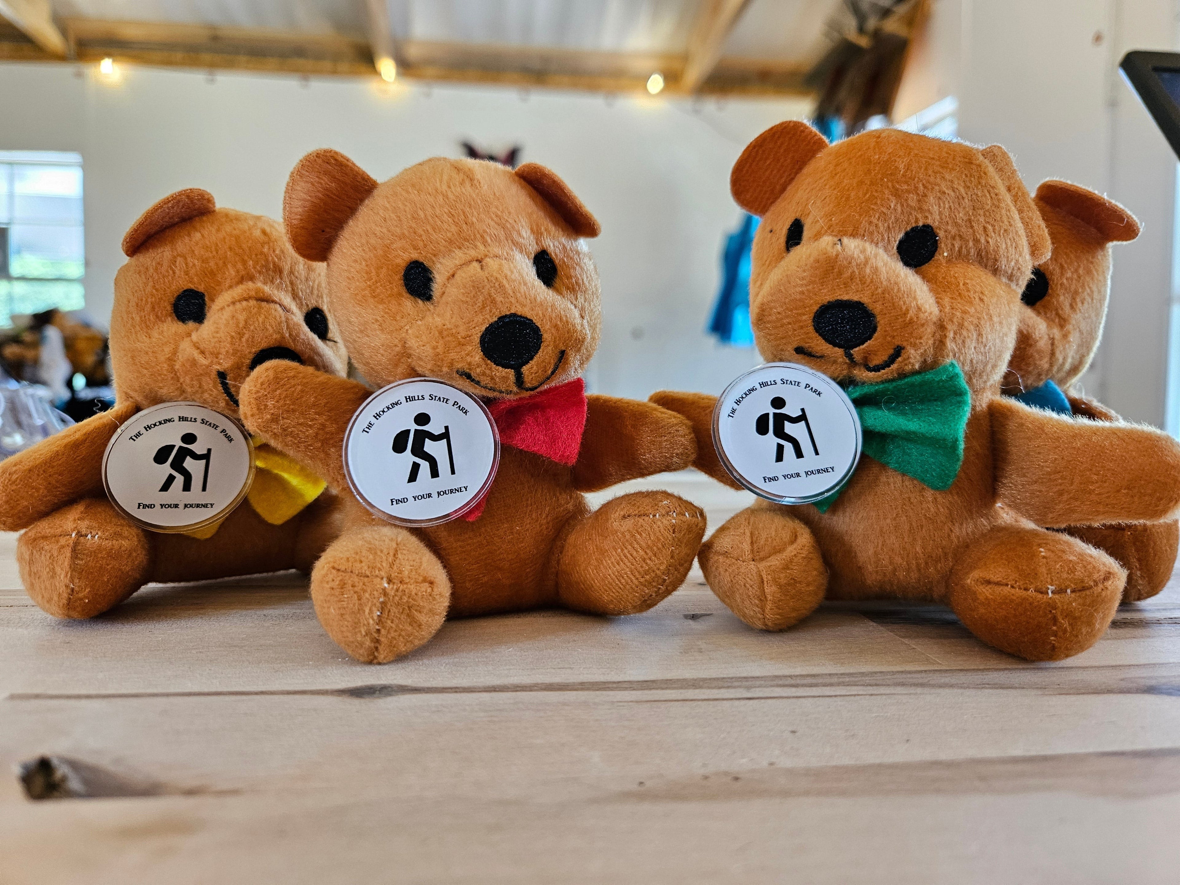The Hocking Hills Store plush teddy bears in brown with red, yellow, and green bow ties, each with a park logo pin.