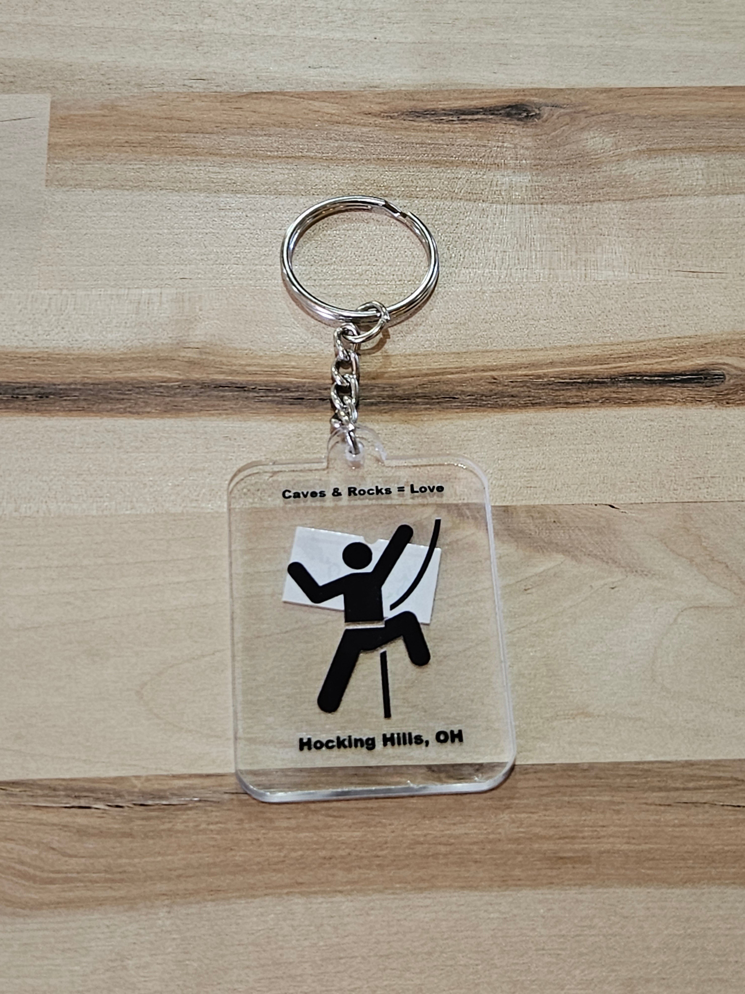 The Hocking Hills Store keychain features a clear acrylic design with a black silhouette of a rock climber and text 'Caves & Rocks = Love' and 'Hocking Hills, OH'.