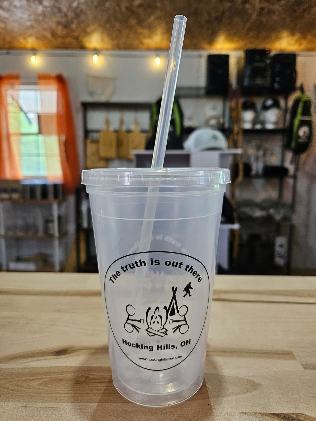 The Hocking Hills Store clear plastic sipper cup with lid and straw, featuring a Bigfoot and campfire graphic.